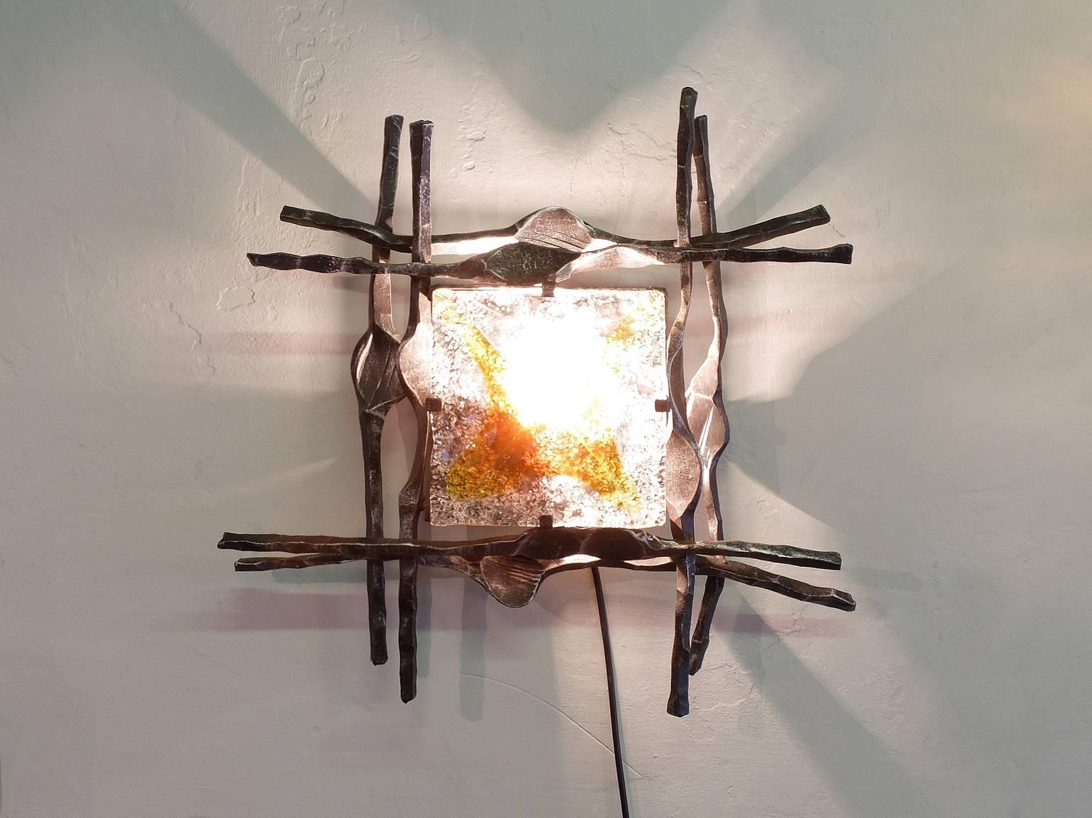 A large wall sconce from Swedish design company A & E Design, circa 1970, in the Brutalist style. The hand-wrought iron surround has a good patination and is set off by the Mazzega Murano glass with clear and amber tones. This wall light has been
