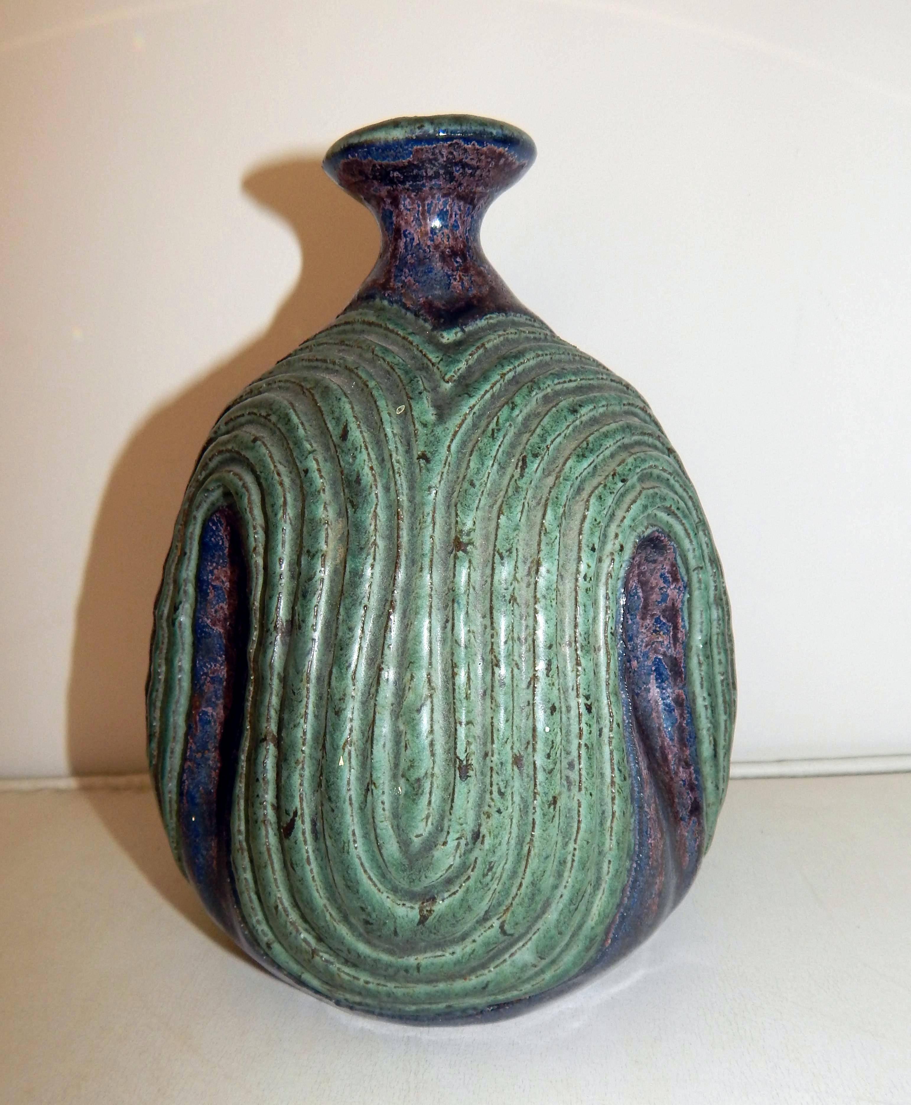 Green stoneware bottle with undulating carved design.
Underlying mauve and blue accents.
Marked on the base: MKG.
By well-known designer and craftsman, Maurice K. Grossman
from Arizona where he taught at the University of Arizona, Tucson for