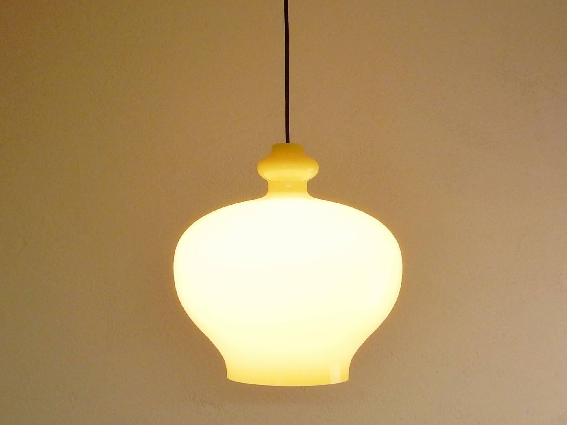 This bright yellow glass pendant light is in a great condition. This model was made in two sizes of which this light is of the larger size. The glass has a white opaline inside and is bright yellow on the outside. This gives a great softened light