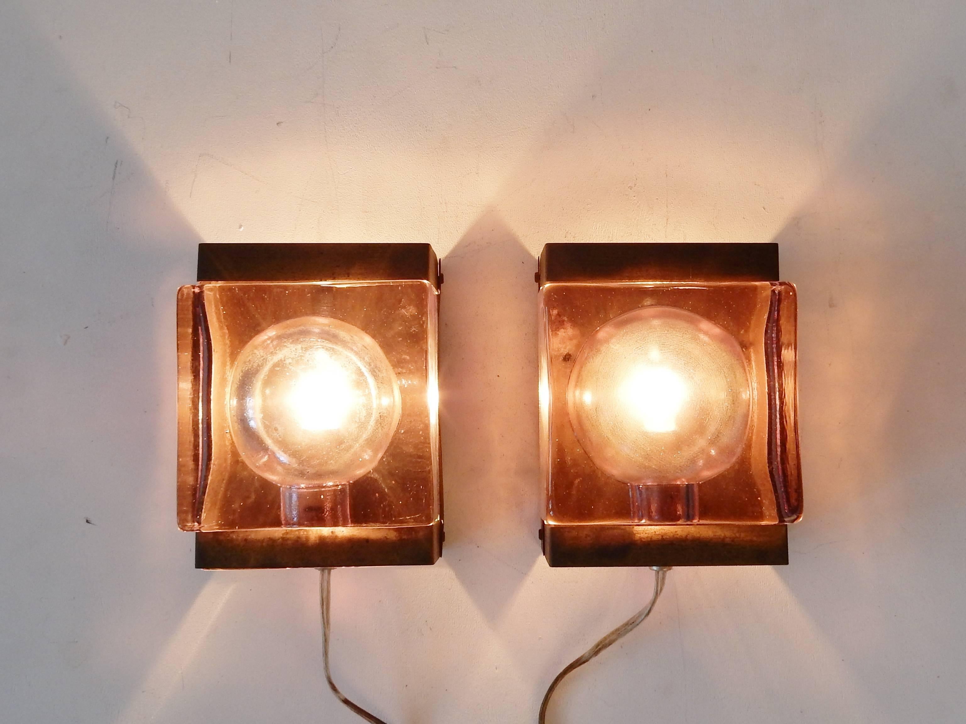 This set of two wall lamps are of purple or pink tone colored glass. A thick and heavy glass that gives a lovely effect and spread to the light. The backside tells us these lights are 