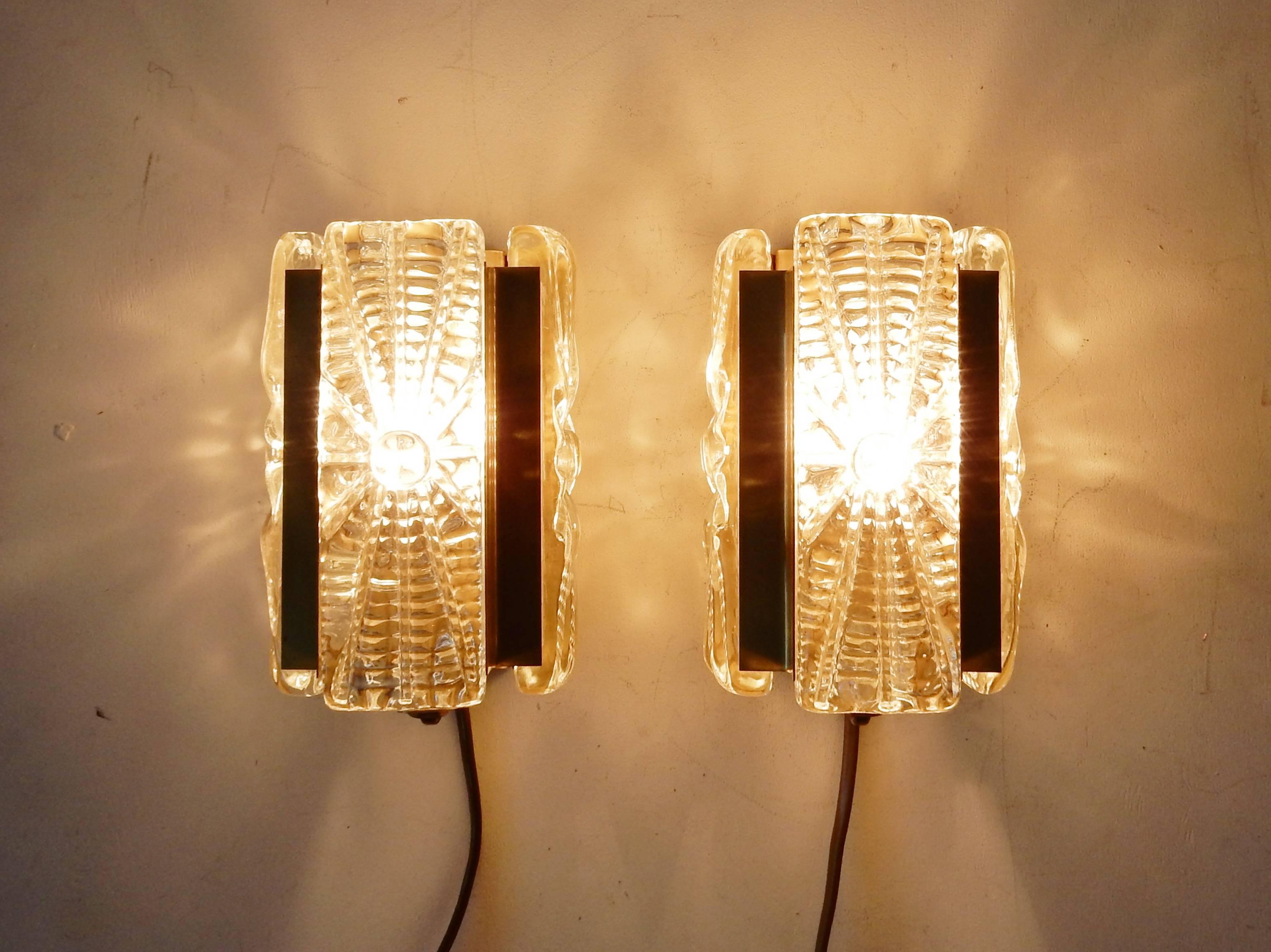 This set of two wall lamps are of a gold colored metal fixture with three thick decorated glass parts. 
Both lights are in very good condition with minor signs of age and use. Both are labelled on the back.