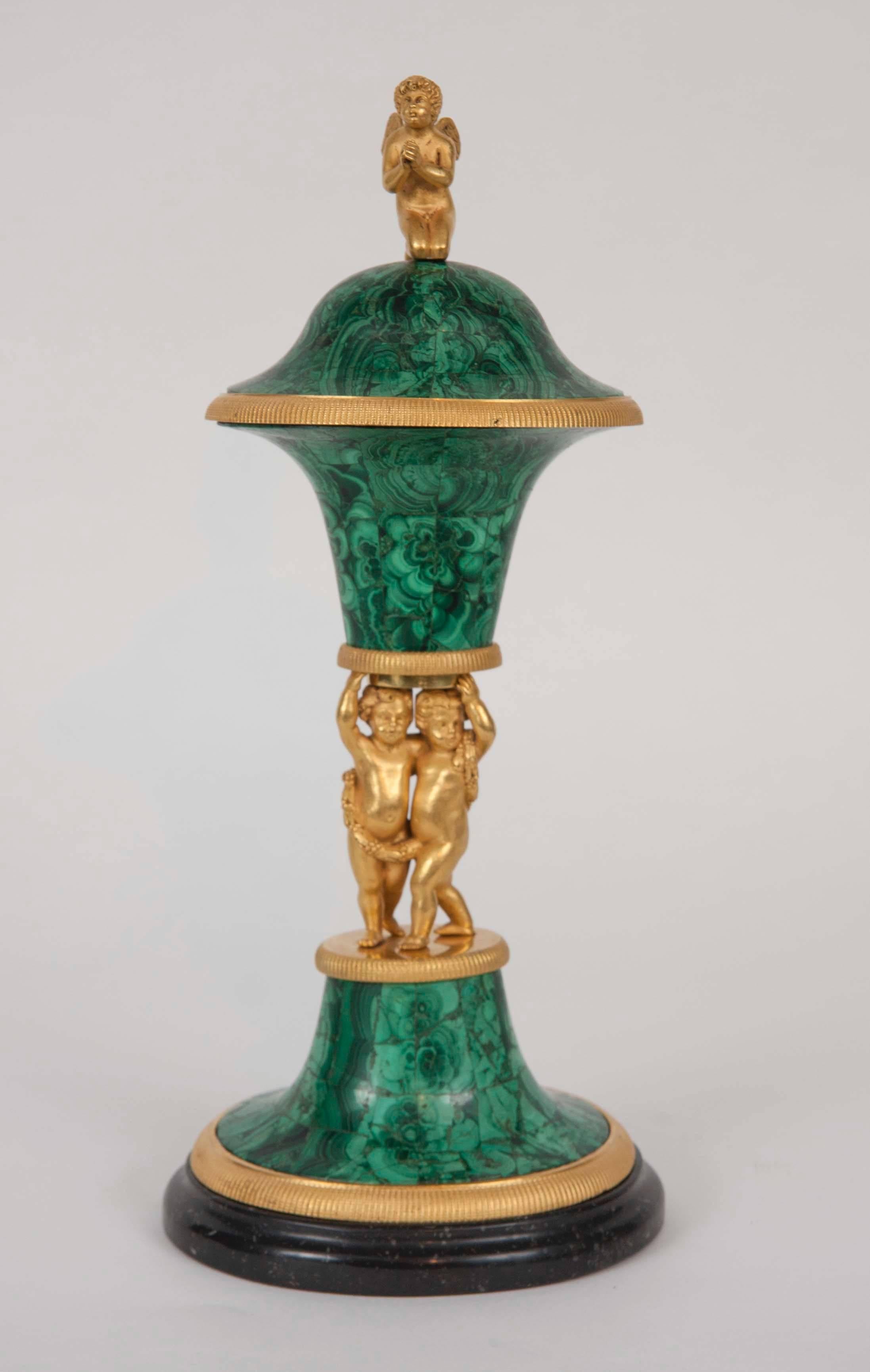 A Russian gilt bronze and malachite covered vase on porphyry base.
Form of winged cupids supporting a malachite vase.
Russia, circa 1800.
Height 14 in.

A similar piece sold at Sotheby's London (December 7, 2010 Important Furniture, Silver &