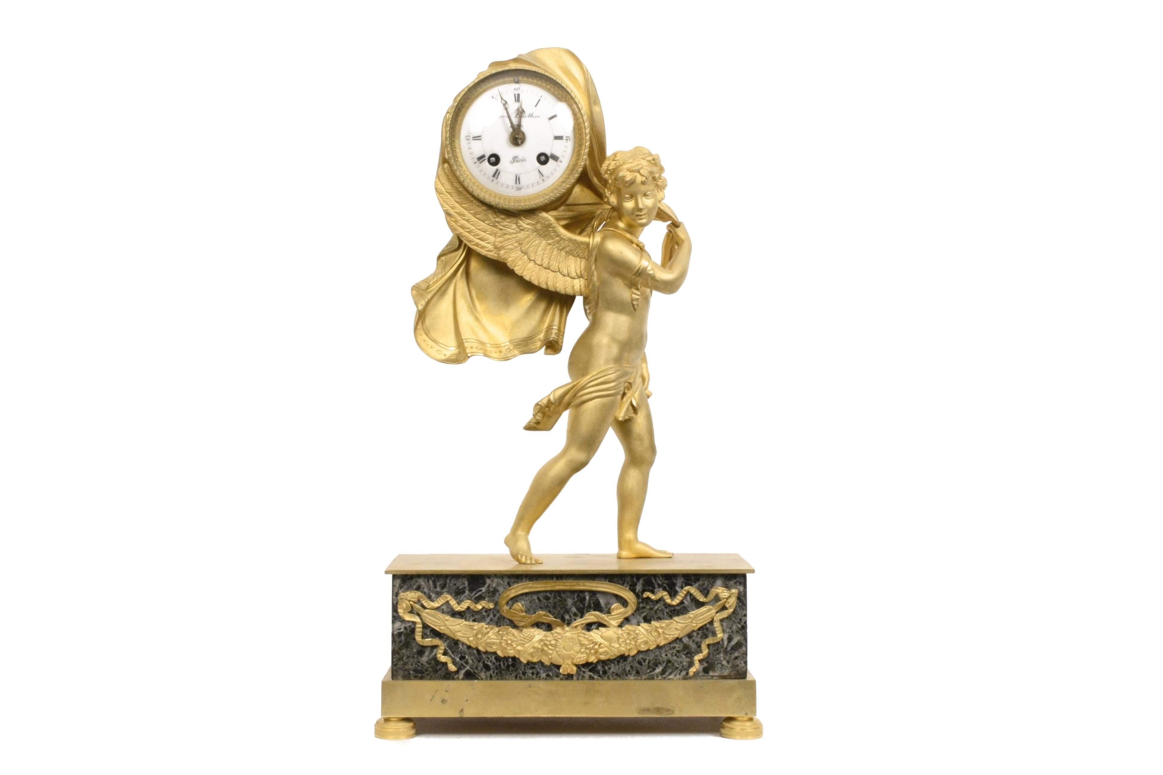 Winged cupid with flowing robe, clock resting between wings and fabric, raised on bronze ormolu-mounted verde antico plinth. 
France, first half of the 19th century.

Measures: H 16 in.
