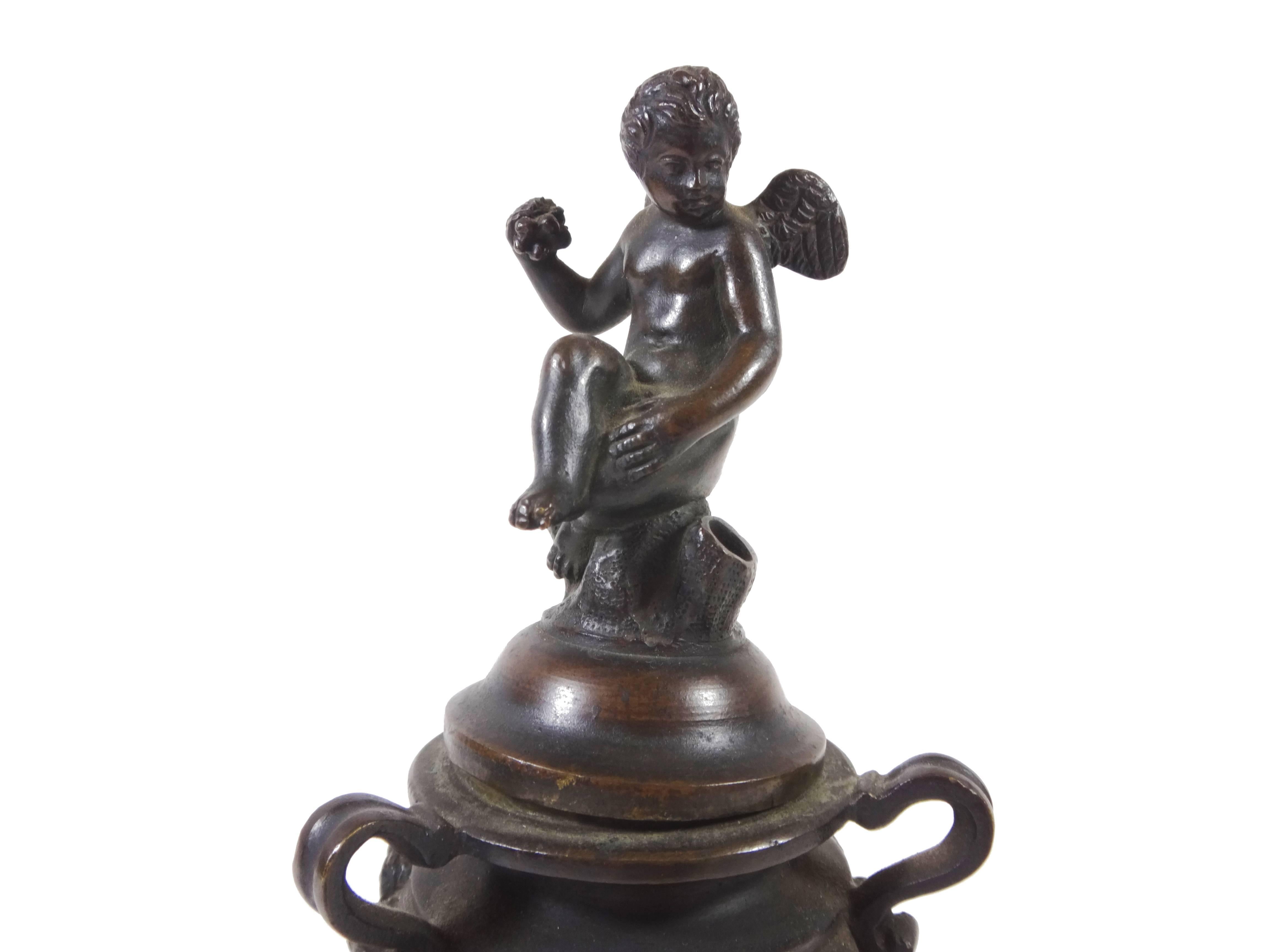 Patinated bronze urn-shaped inkwell rests on three winged-horses evoking movement and action. The body of the inkwell is decorated with faces among garlands and the lid is topped by a seated putti holding fruitVenetian patinated bronze figural