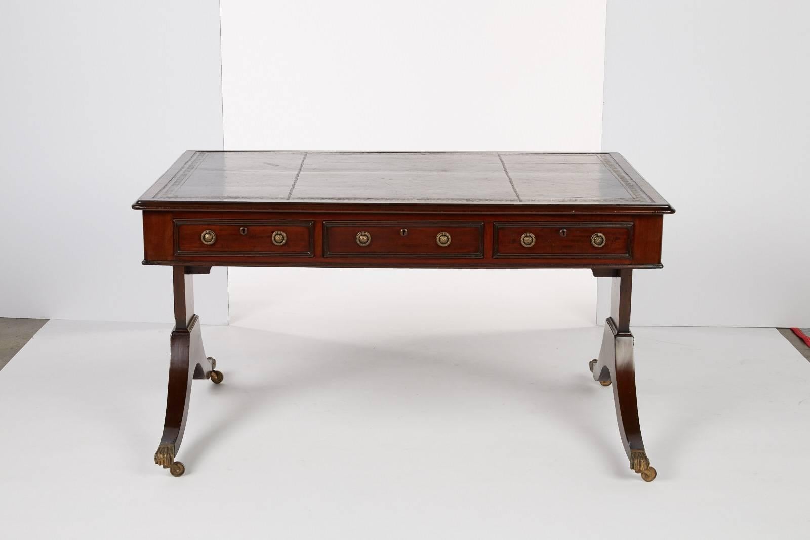 An early 19th century French mahogany bureau plat with embossed black leather top. This desk has brass paw foot casters.