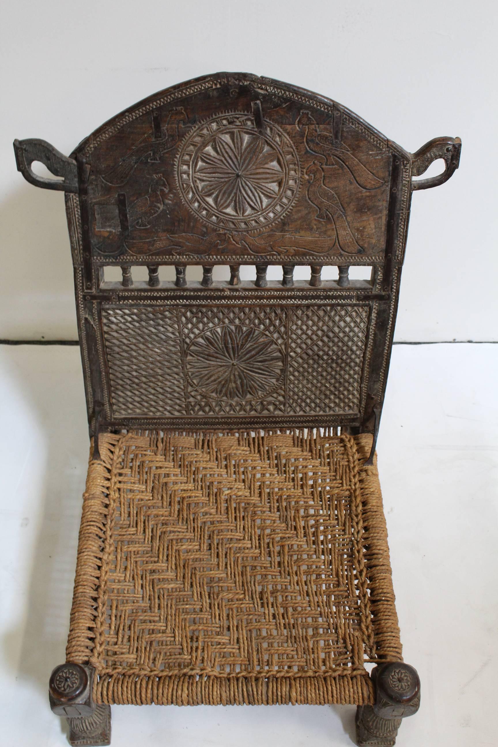 Hand-carved antique Afghan chieftain chair. Ornate patterns and birds carved in front with two bird heads on side. Handwoven rope seat. Antique iron repairs.