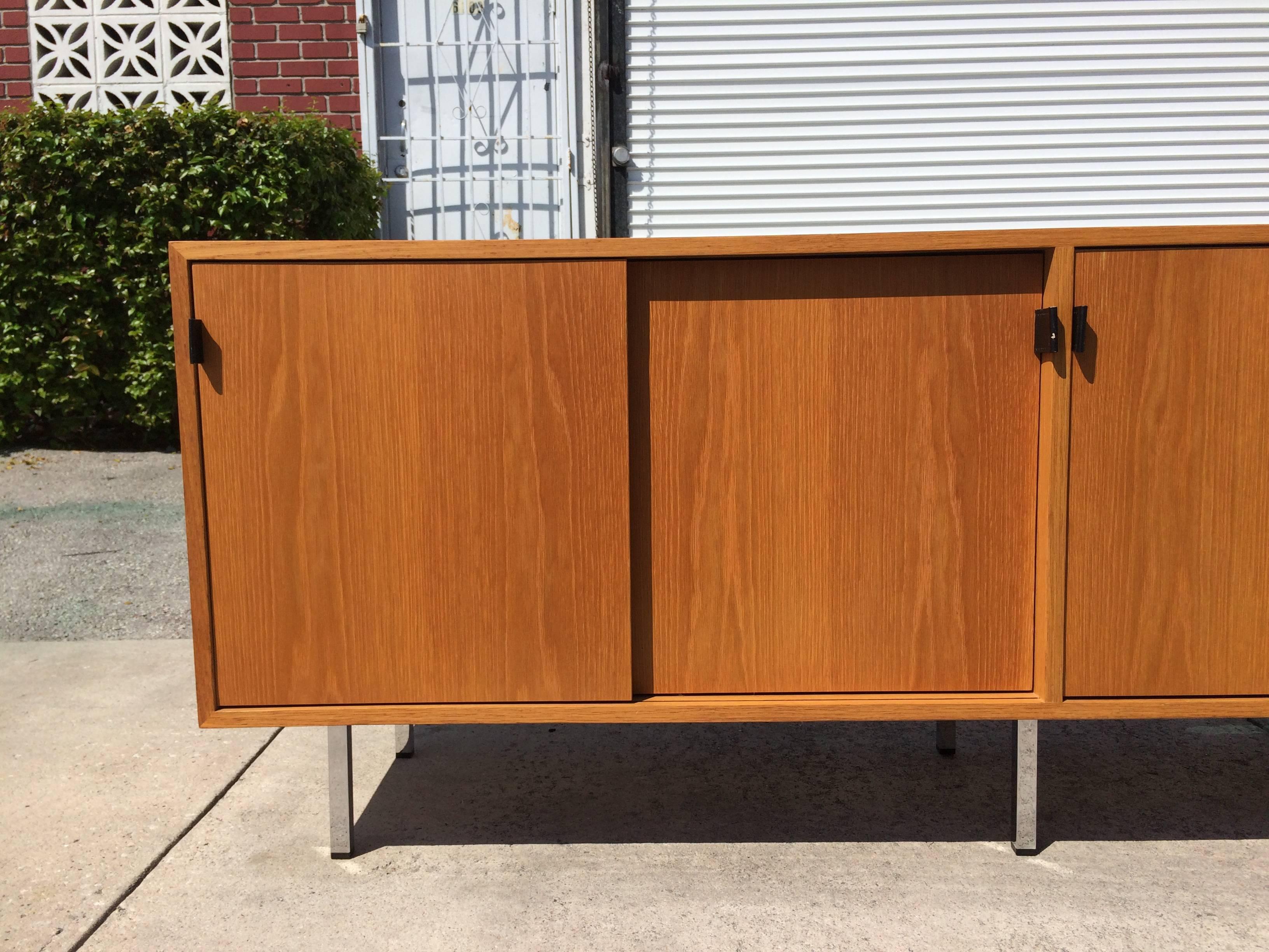 Credenza on six chrome legs, four sliding doors with black leather pulls. Behind the sliding doors are six shelves.