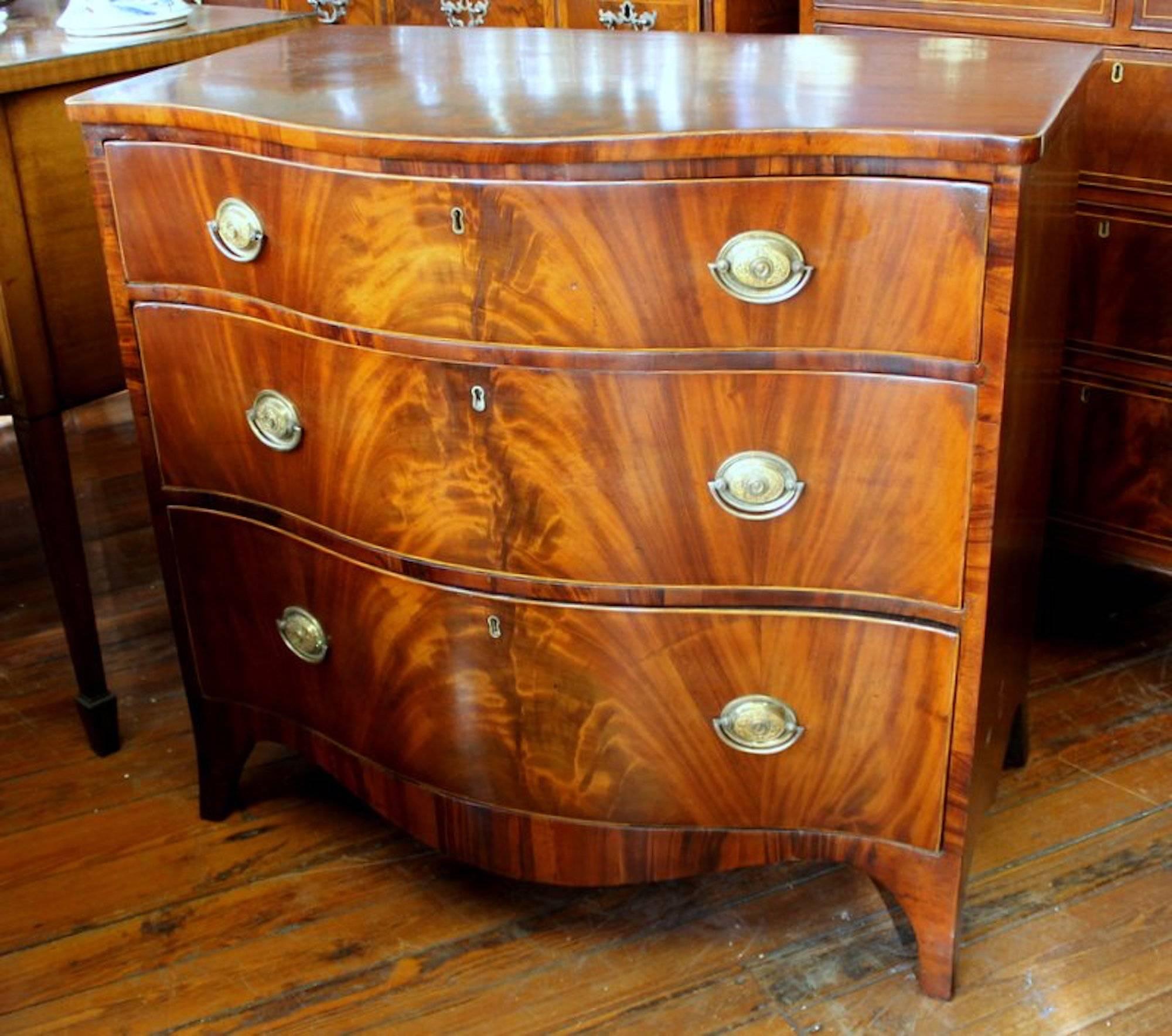 Fabulous and rare antique English George III PERIOD flame or bookmatched figured mahogany Hepplewhite style serpentine chest of drawers

Oval ormolu brasses are antique. 

Please note holly line inlay around edge of top and drawers.
(A couple of old
