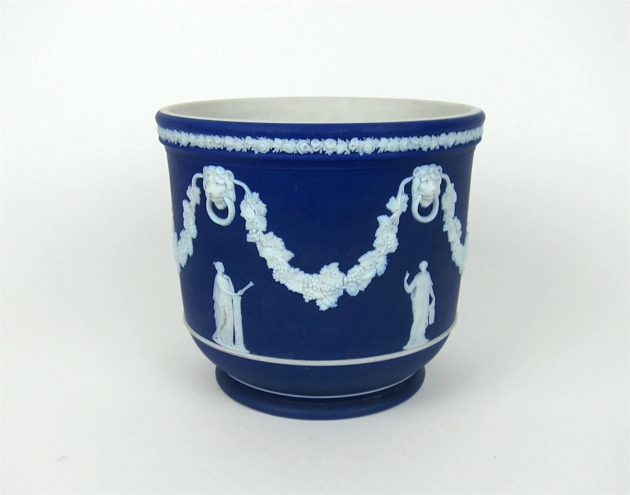 A large, antique Wedgwood Jasper dip cache pot or jardiniere in dark cobalt blue with a contrasting white interior and neoclassical style ornament applied in relief. The exterior is decorated with an intricate floral border encircling the rim, white