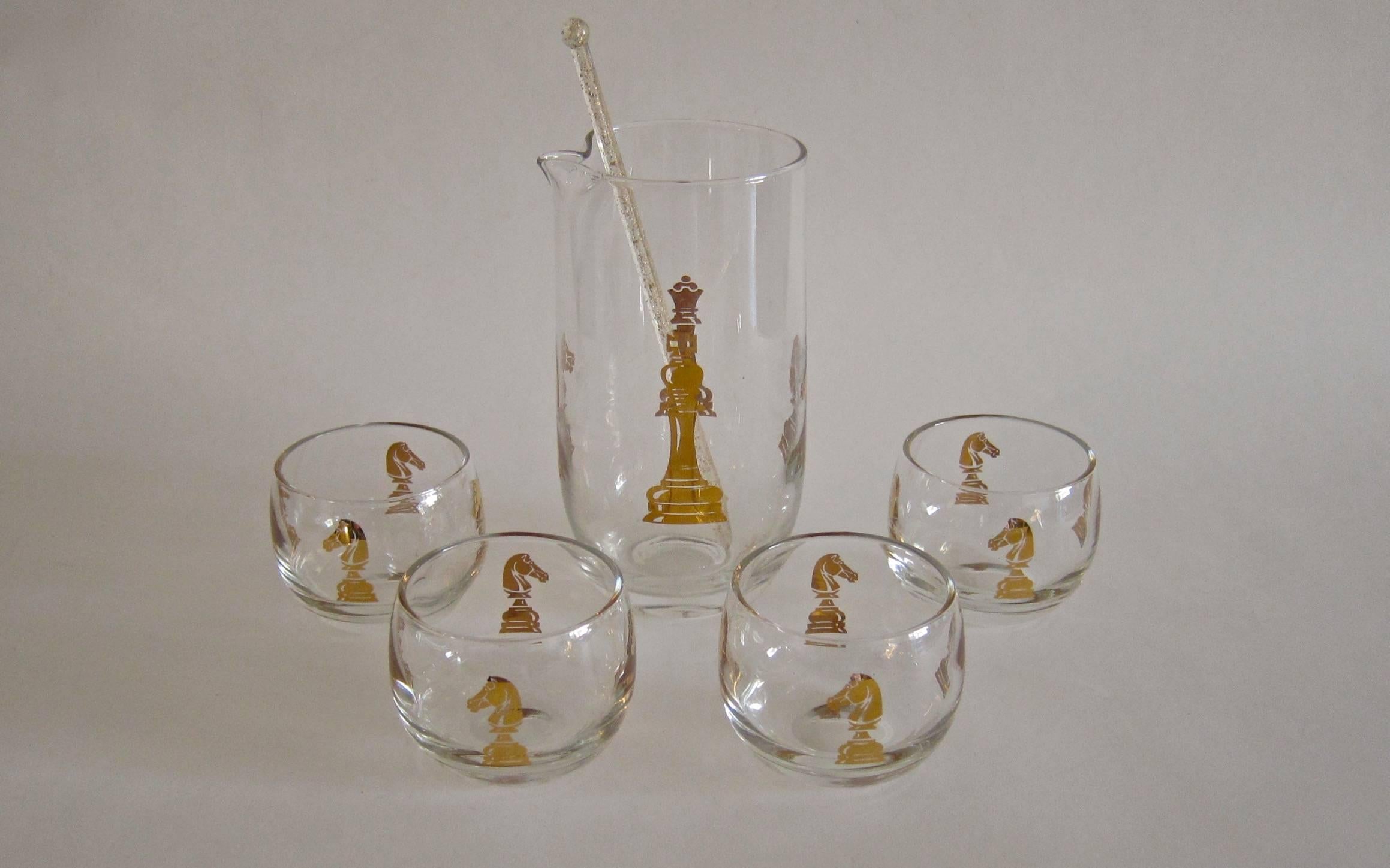 A chess-themed vintage glass cocktail set with original box comprised of six pieces: A pitcher decorated with a golden king, queen and knight, a stirrer and four matching roly poly glasses decorated with golden knights. The set was manufactured by