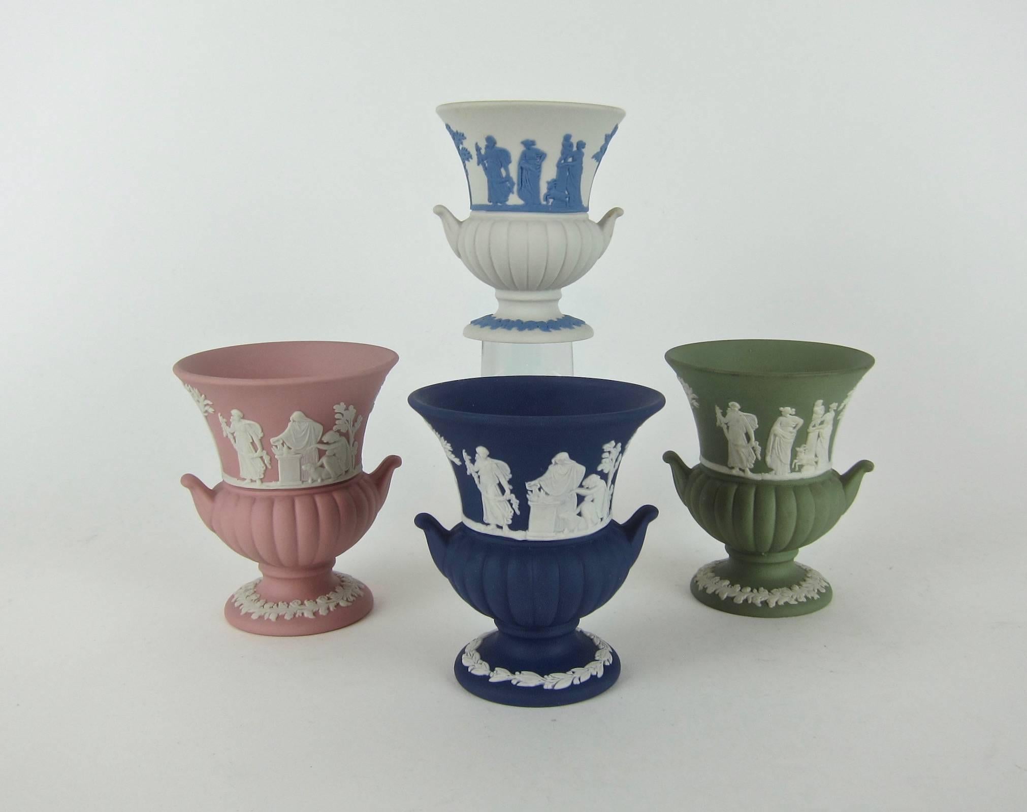 A colorful vintage collection of four small urns in white, sage green, pink, and Portland blue solid Jasperware from Wedgwood of England. The vessels were produced in 1964, 1974, 1978, and 1982.

Each decorated with neoclassical bas-relief figures,