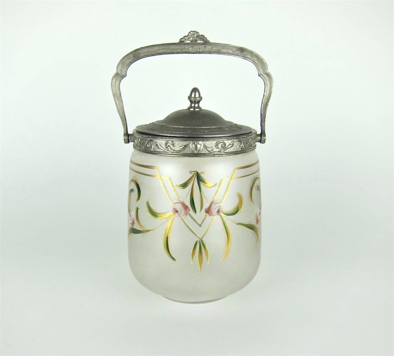 An antique biscuit jar of frosted, satin glass with a silvered metal rim, removable top, and bail handle dating to the late 19th-early 20th century. The body is skillfully decorated in raised enamels in the Art Nouveau / Jugendstil style. The piece