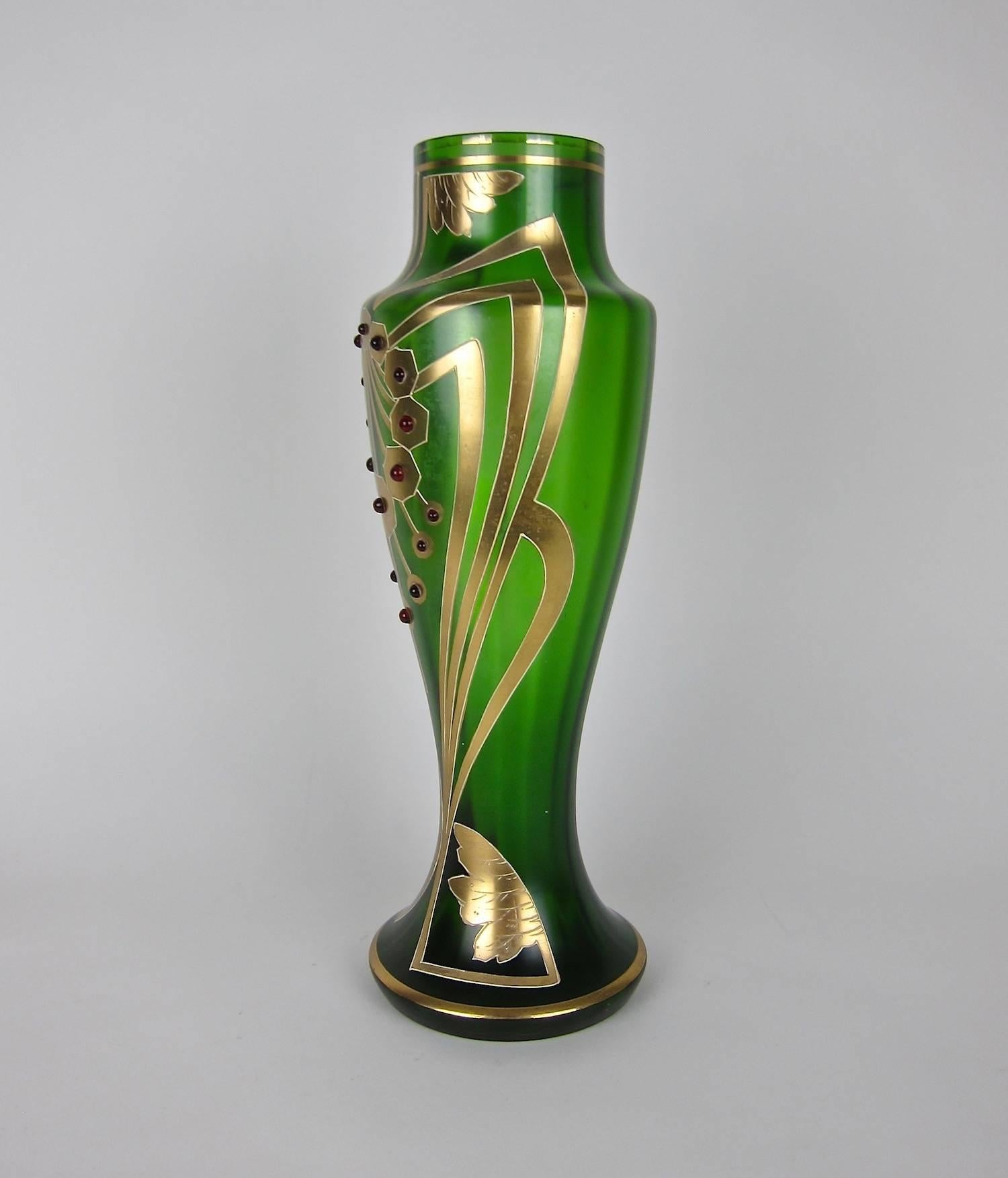A tall and striking Bohemian art glass vase, dating circa 1900-1905. The ribbed, green glass vessel was mould-blown and includes a starburst pattern on the base. The hand painted gold work decoration features an Art Nouveau / Jugendstil whiplash
