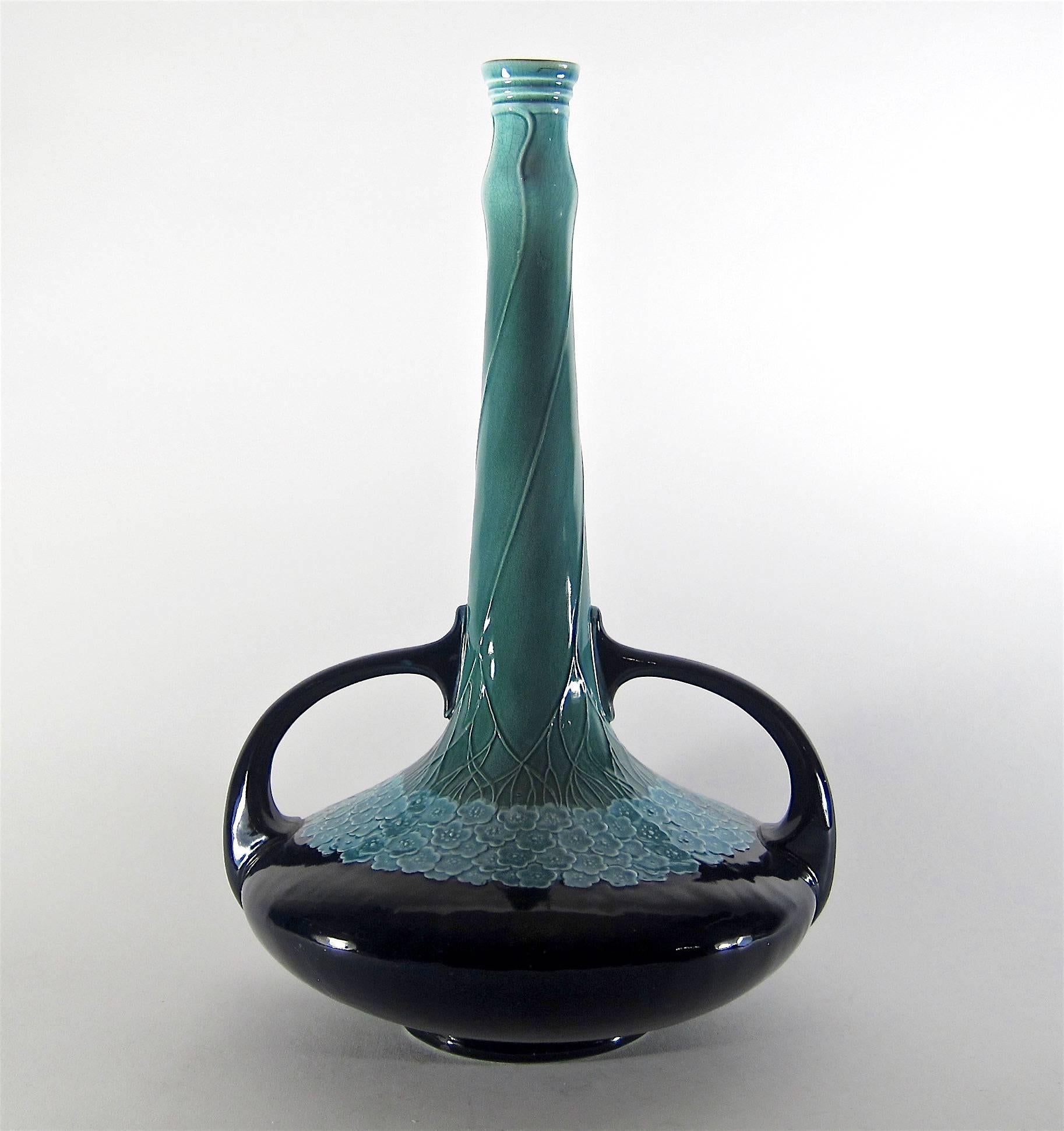 A tall antique double handle vase made in 1904 at the height of the Art Nouveau period at the Villeroy & Boch factory in Mettlach, Germany.

The interior of the vessel is glazed in pale green, the attenuated neck transitions from aqua to teal