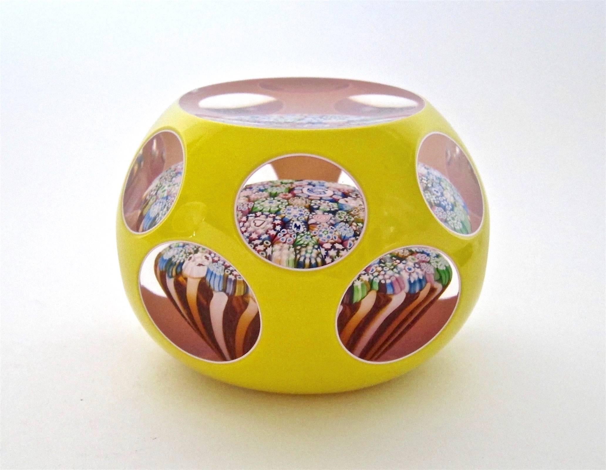A handcrafted studio glass paperweight by John Deacons of Scotland, designed with a double overlay of bright yellow over white with cut round and oval facets. Closepack millefiori design with Silhouette canes including a rooster, bird and dog and a
