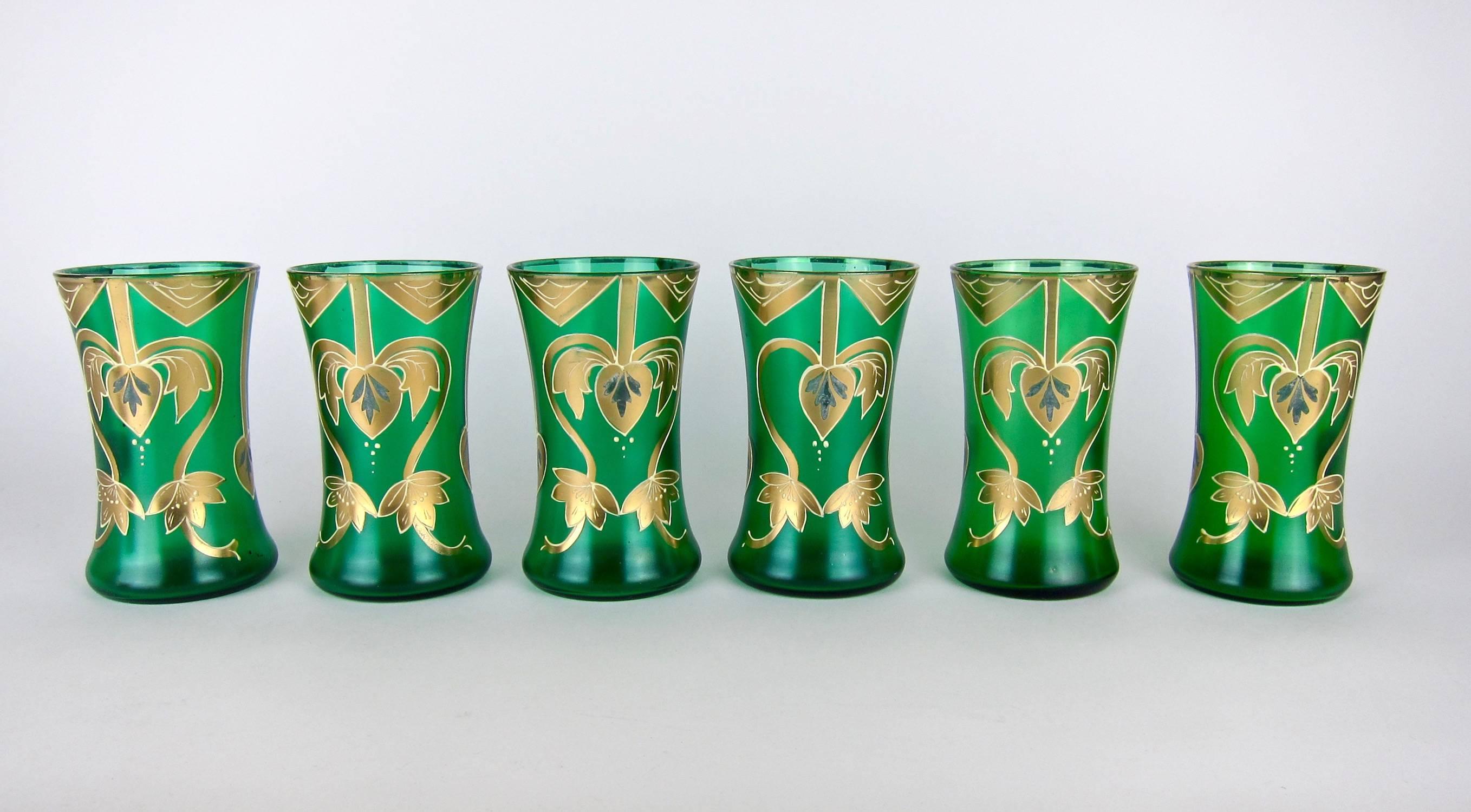 Antique set of six drinking glasses in emerald green satin glass. Each glass is decorated with a gilt rim and raised, hand-painted enamel in the Art Nouveau / Jugendstil style. The glasses are unmarked, but were made in Bohemia, an area encompassing