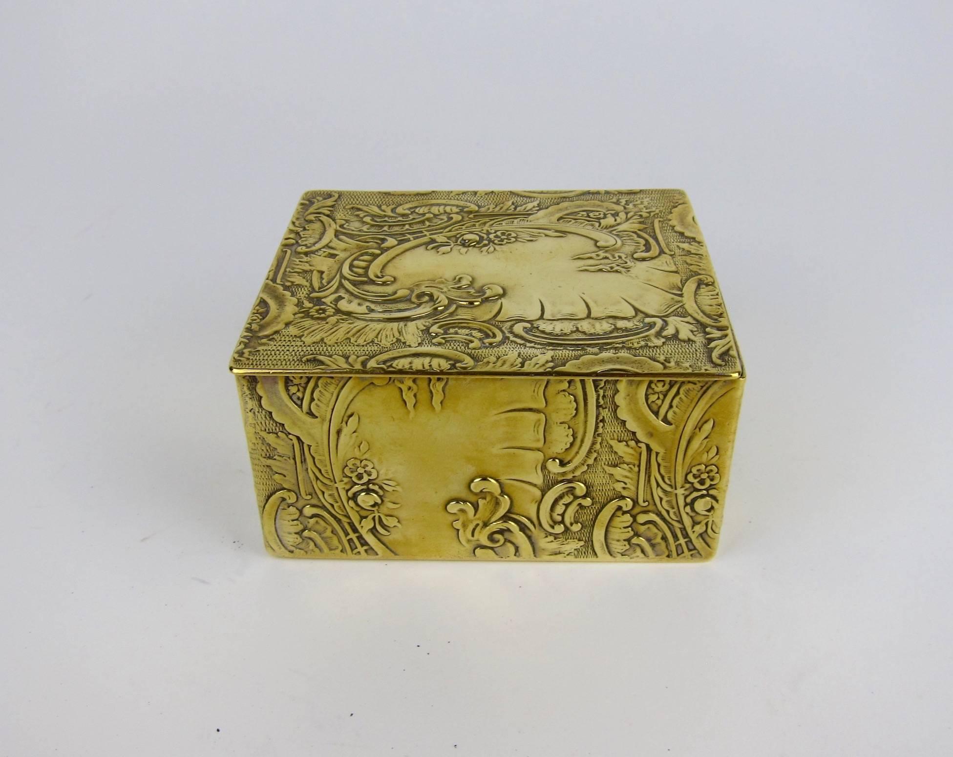 This exquisite decorative box, originally designed to hold cigarettes, is perfectly sized for use as a jewelry casket or as an ornamental accessory for a desk, bedside, or vanity table. 

The Rococo Revival design of embossed brass features low