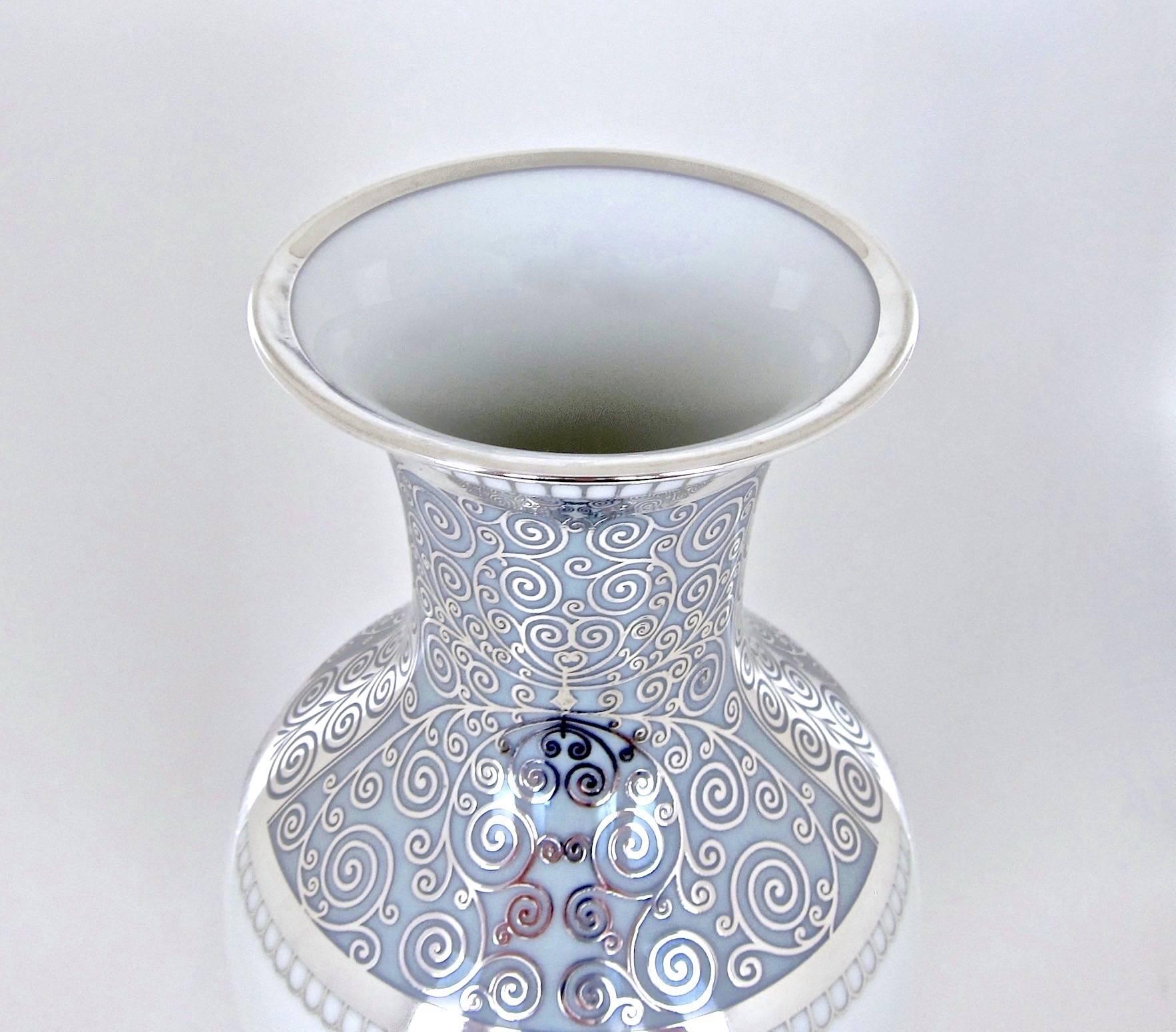 A large vintage Rosenthal porcelain vase ornamented with an elegant, overlay design of pure silver handcrafted in Germany between 1953 and 1956. The silver overlay work consists of spiraling tendrils with two silver bands at the rim, one at the