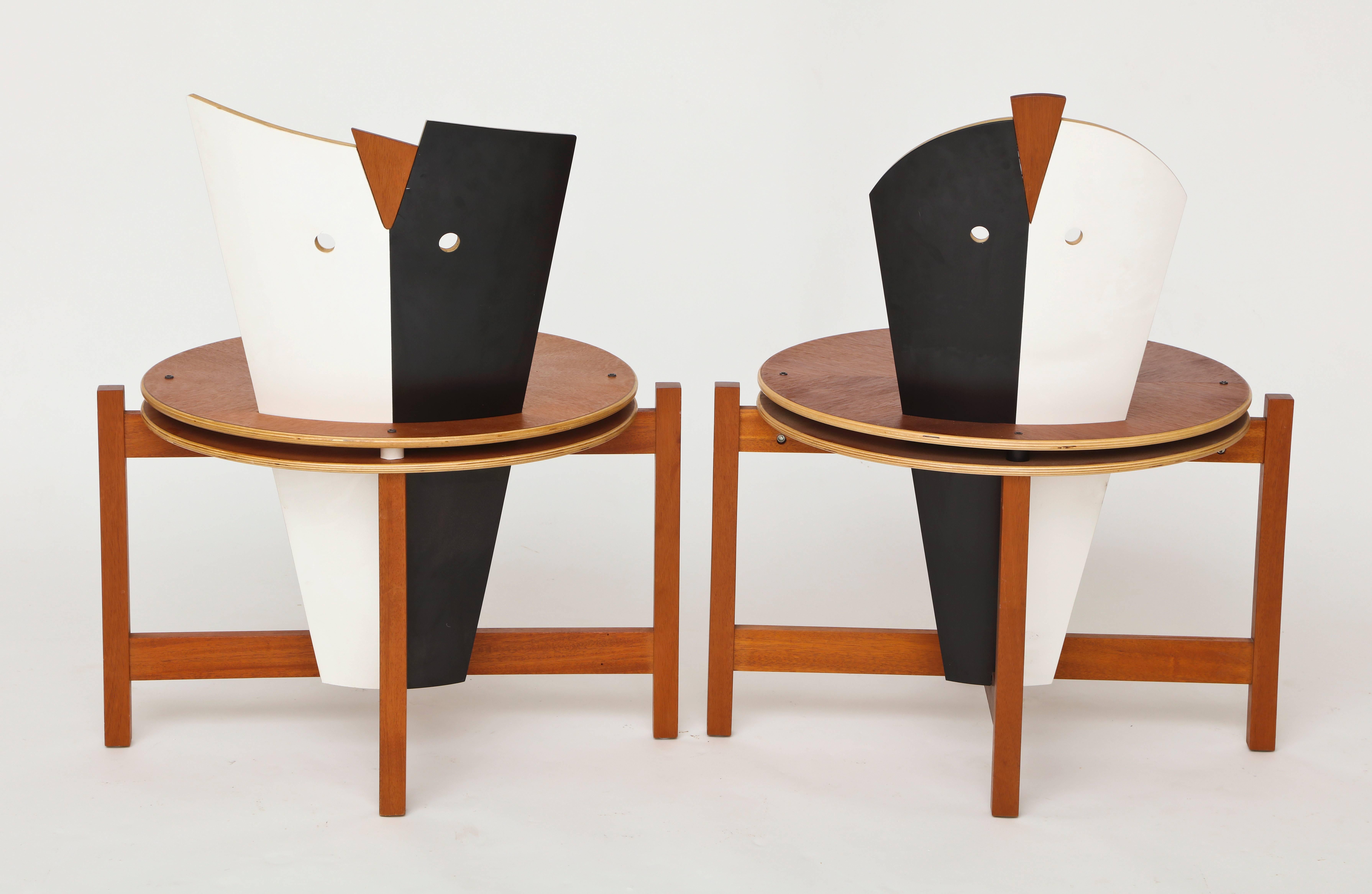 Robert Evanson Post Modern 1980 Chairs Tables Pair Modernist Memphis

Modernist pair of chairs or tables.
Stained and painted wood chairs. Back of chairs form a stylized mask. Circular seats and rectangular back legs are joined with a stretcher