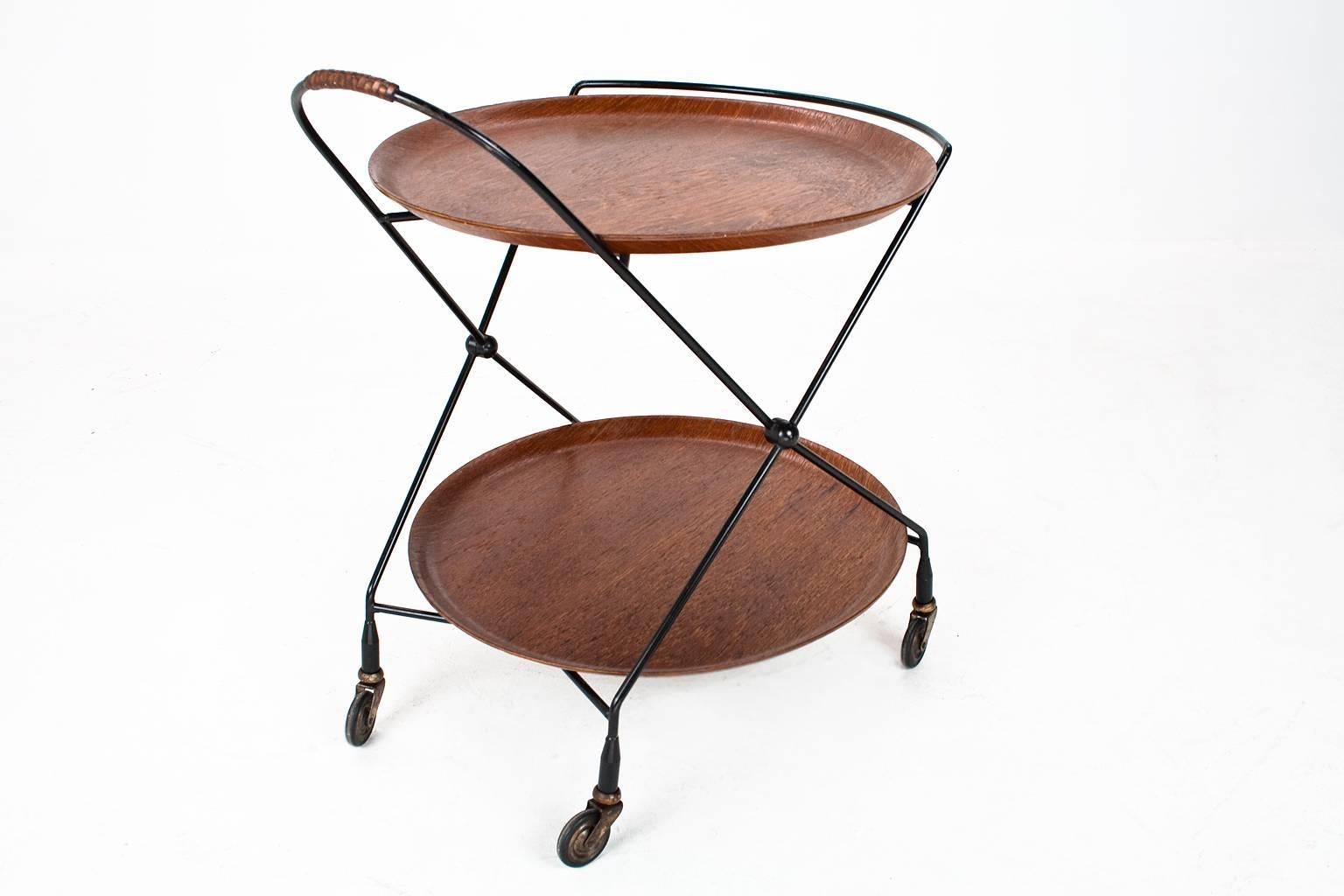Beautiful Swedish Mid-Century Modern serving table, trolley with two teak wooden serving trays on a black lacquered metal frame with four rotatable wheels. 

The trolley is foldable as shown on last photo. This piece considering the age in