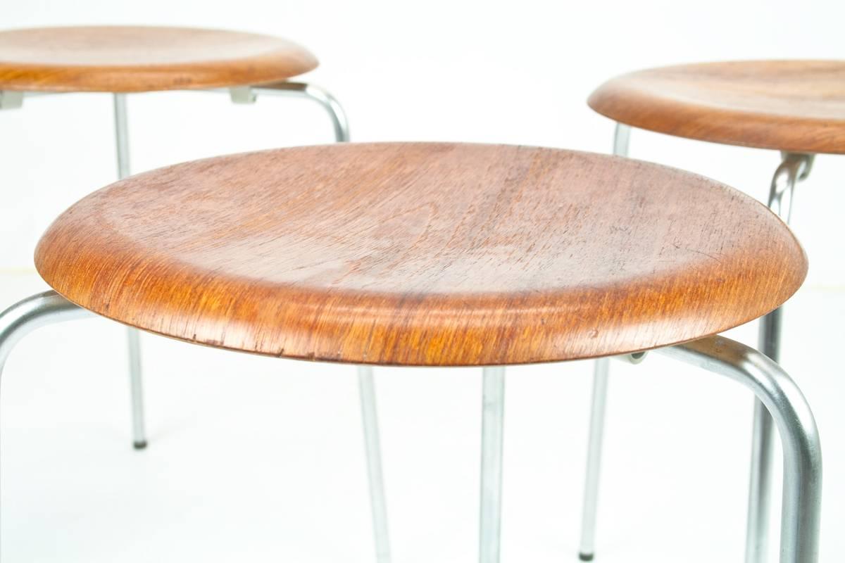 Three very early 1950s teak Arne Jacobsen DOT stools in teak and chrome. The stools have an asymmetrical base with the three chromed feet. 

Made in Denmark by Fritz Hansen. Brand present. Teak seating with chromed legs. Good condition, original