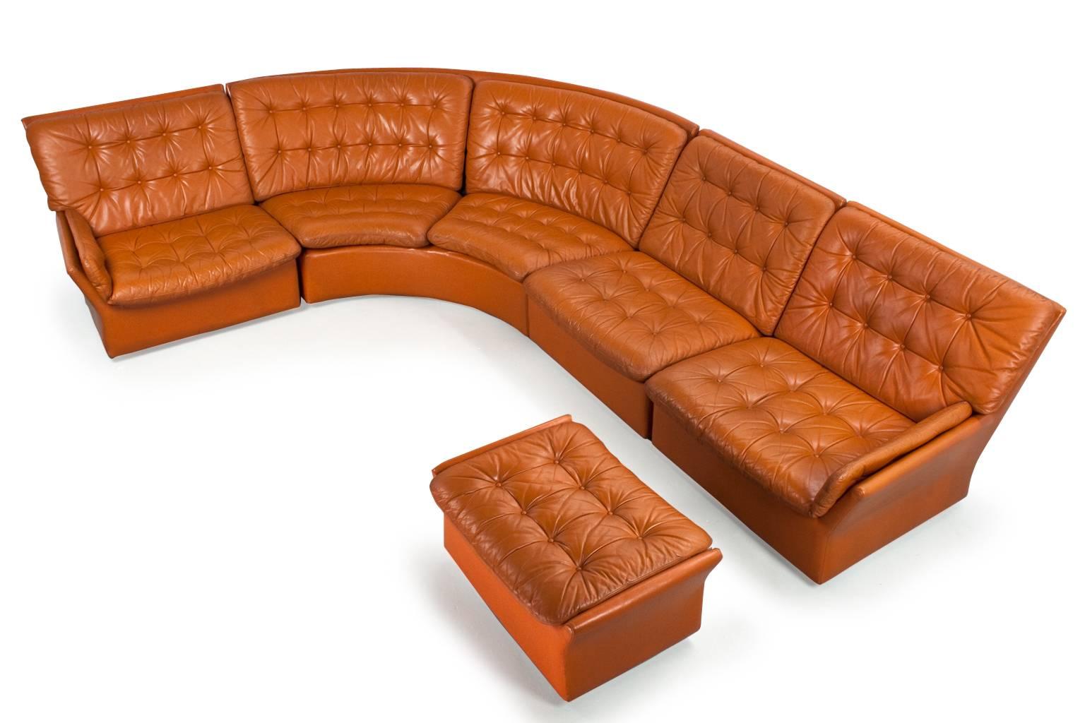 Mid-Century Modern four-sectional corner / round sofa in cognac, brown colored leather, padded upholstery and additional hocker (on wheels). The item is in original and good condition, patina on the leather conform age. Lounge and comfortable
