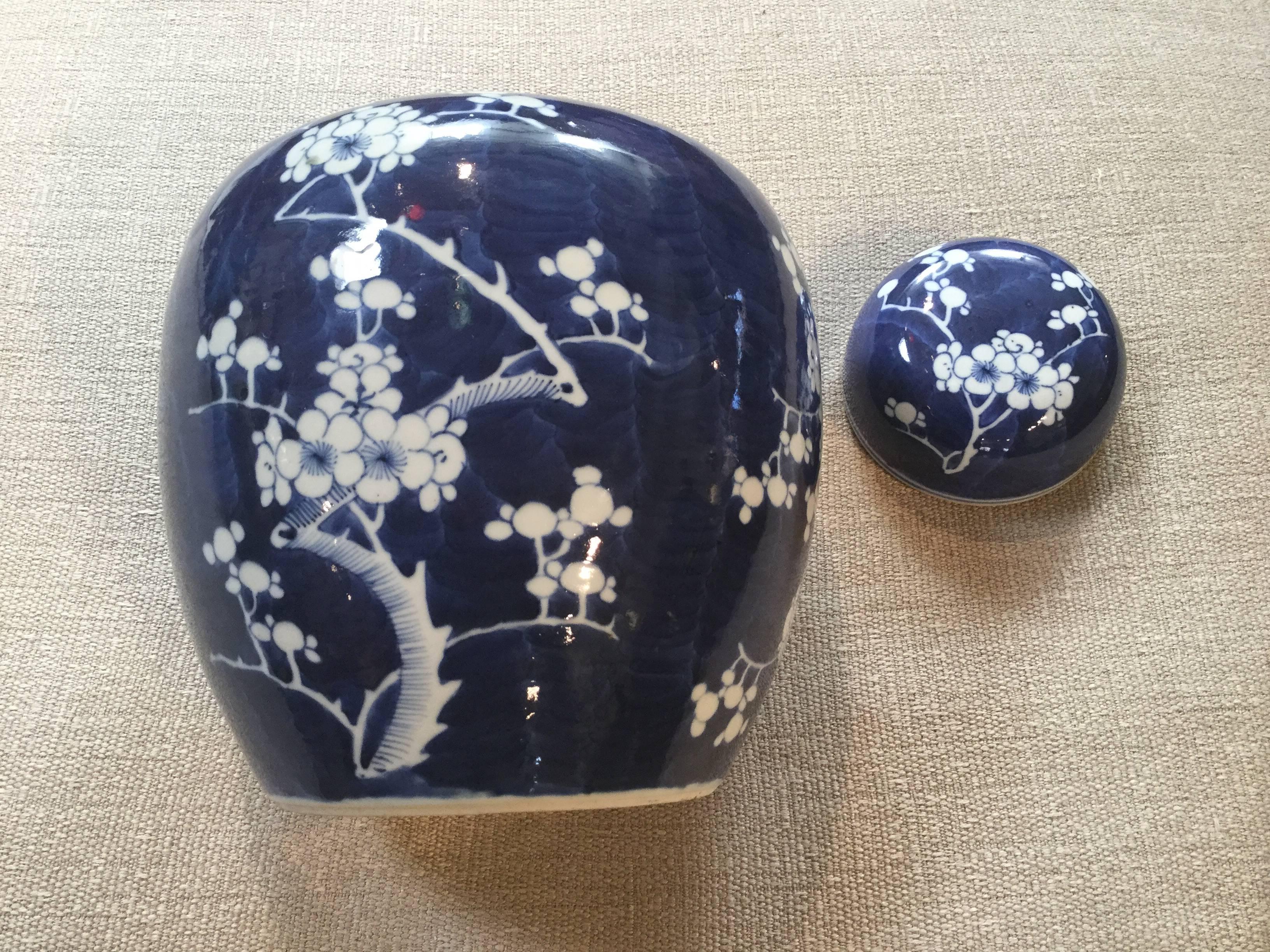 Two beautiful deep blue and white lidded ginger jars on carved hardwood stands. Painted cherry blossom motif showing white porcelains under glaze. Deep blue background brings out the elegant details. One lid has been professionally repaired, almost