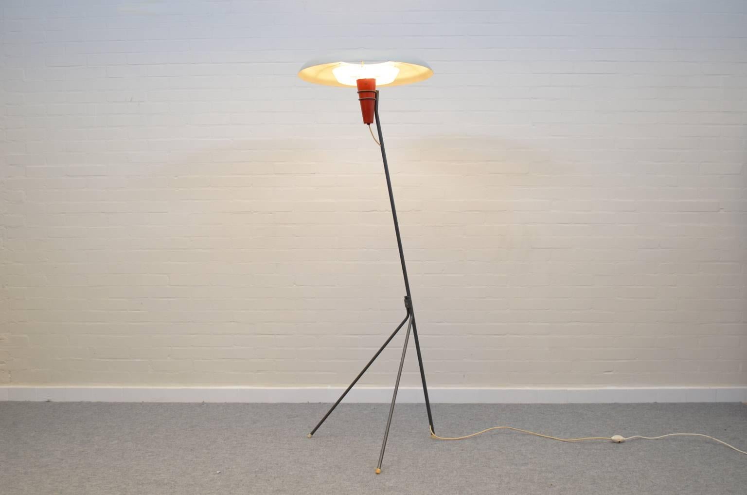 The minimalistic design of the thin wired base ending in a wide turned around scale, gives this floorlamp by Dutch Louis Kalff a futuristic appearance. The lampshade spreads a warm light by using a diffuser. Made of enameled steel in grey, red and