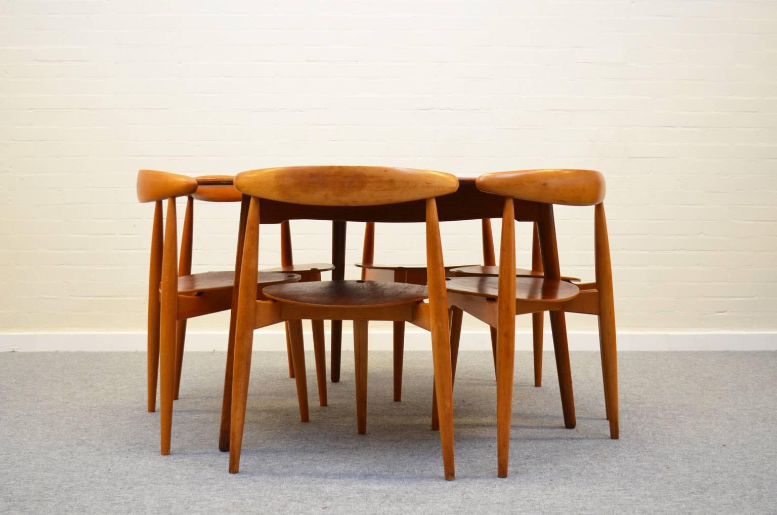 This dining set was designed by Hans J. Wegner for Fritz Hansen in 1952. This one is manufactured in 1964. It consists of a round dining table (diameter 120 cm) and six three-legged Heart chairs made of a combination of teak and oak.