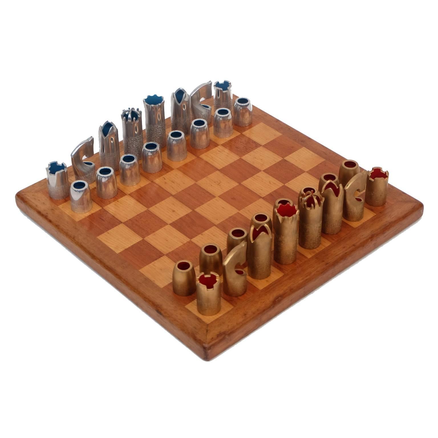 1960s bespoke chess set designed and manufactured in England.

Walnut and sycamore wooden chessboard.

Cast aluminium and gold anodised chess pieces with a textured design.
Orange and blue enamelled interiors.
Complete with original wooden