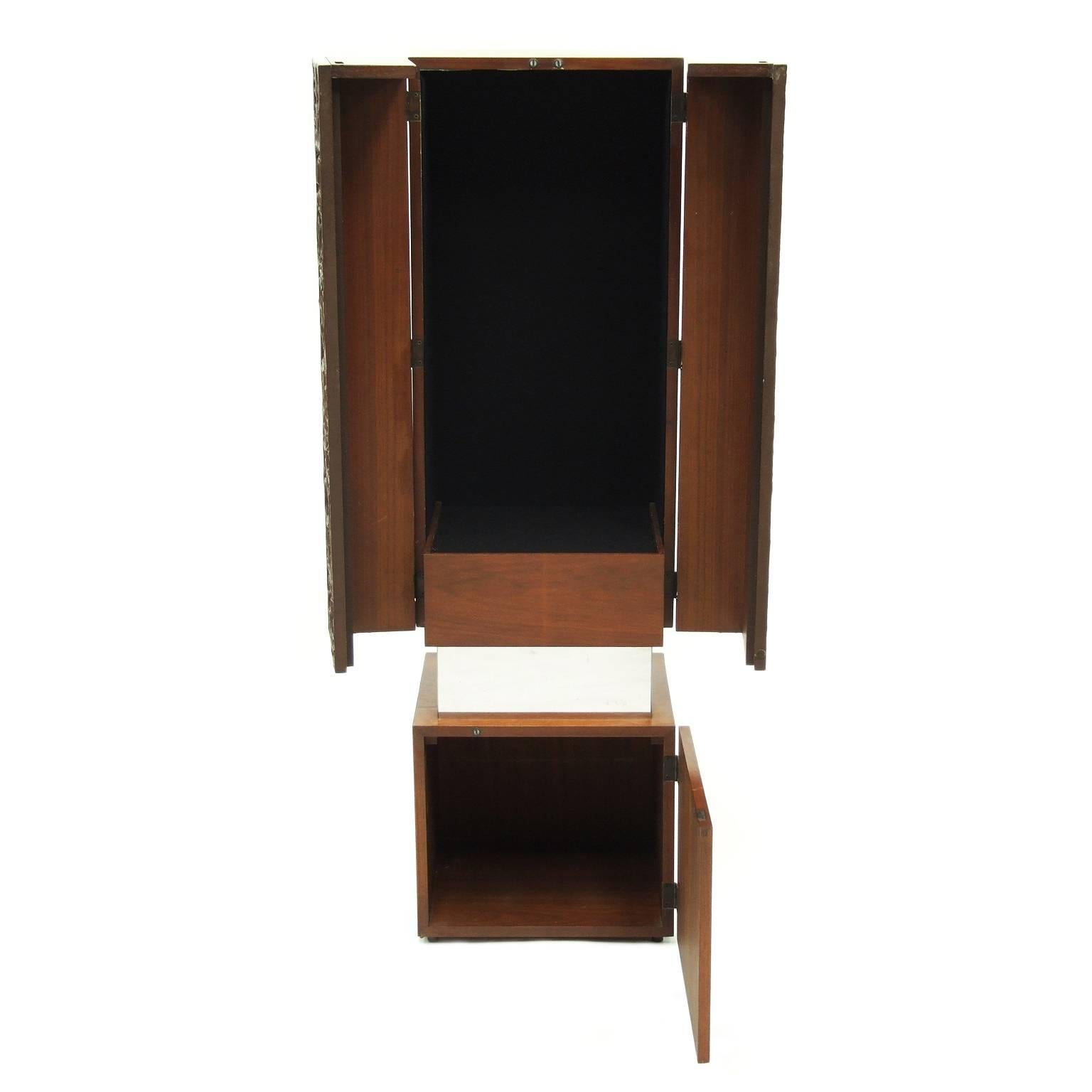 1970s decorative cabinet designed and manufactured in the USA.

Totem design construction with two teak cabinets divided by a polished aluminium plinth.

Black felt interior to top cabinet.

Measures: H 142cm x W 42cm x D 40cm.