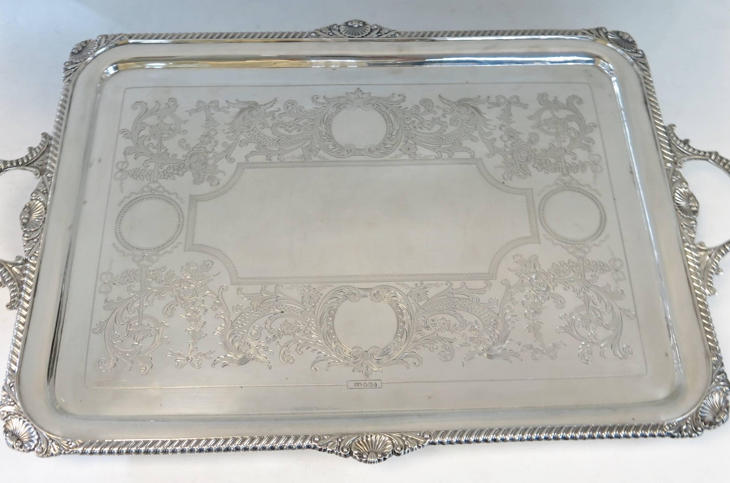 Rectangular sterling silver two handled, footed tray. The surface with hand engraved decoration, the applied border with a shell and gadroon design, matching the cast shell and gadroon handles. Tray stands on four cast gadroon rimmed feet.