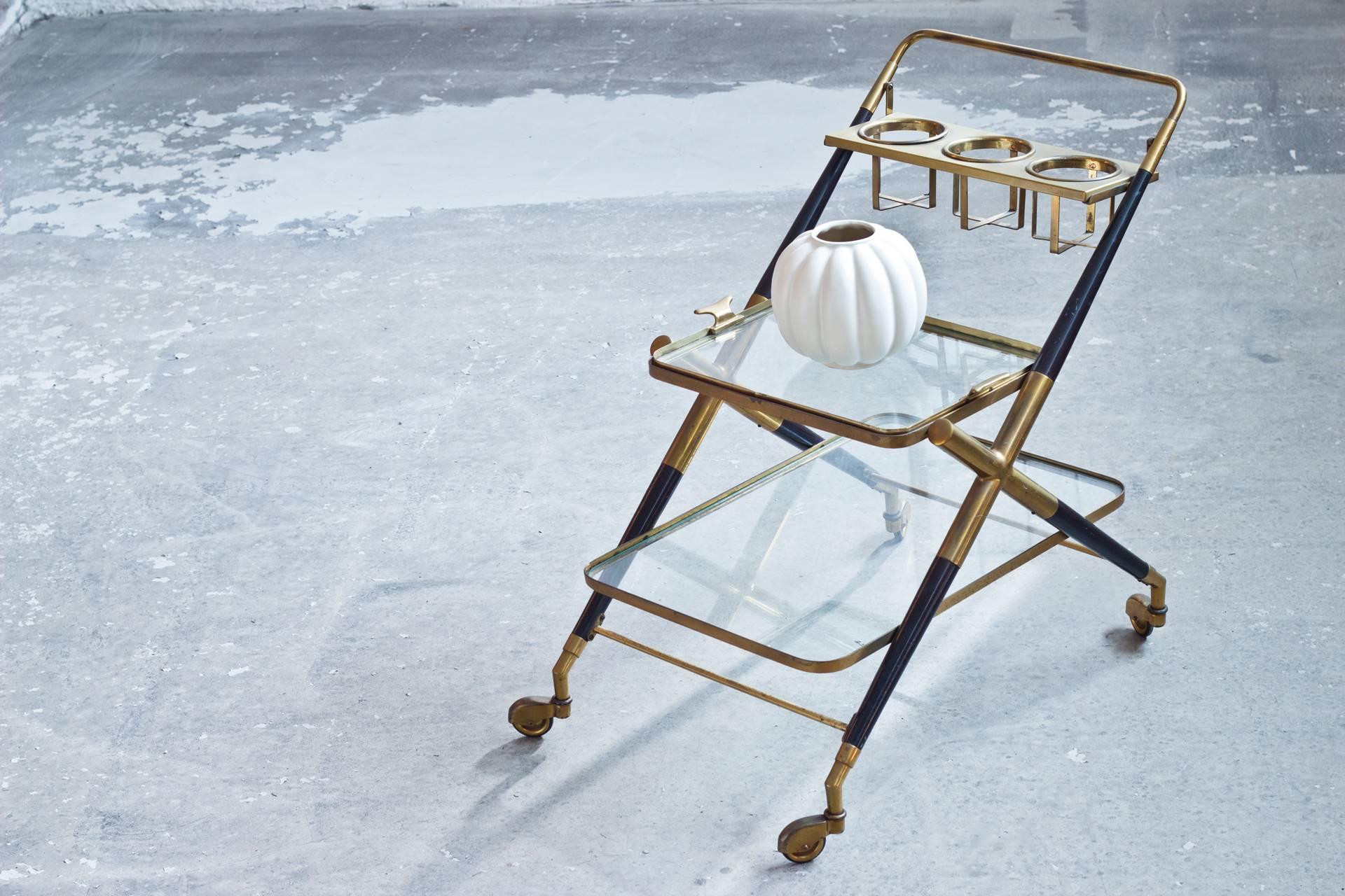 An early edition drinking cart by Cesare Lacca. It is made from brass and black lacquered wood, two glass shelves and three bottle holder. The cart is labeled with a brass tag 