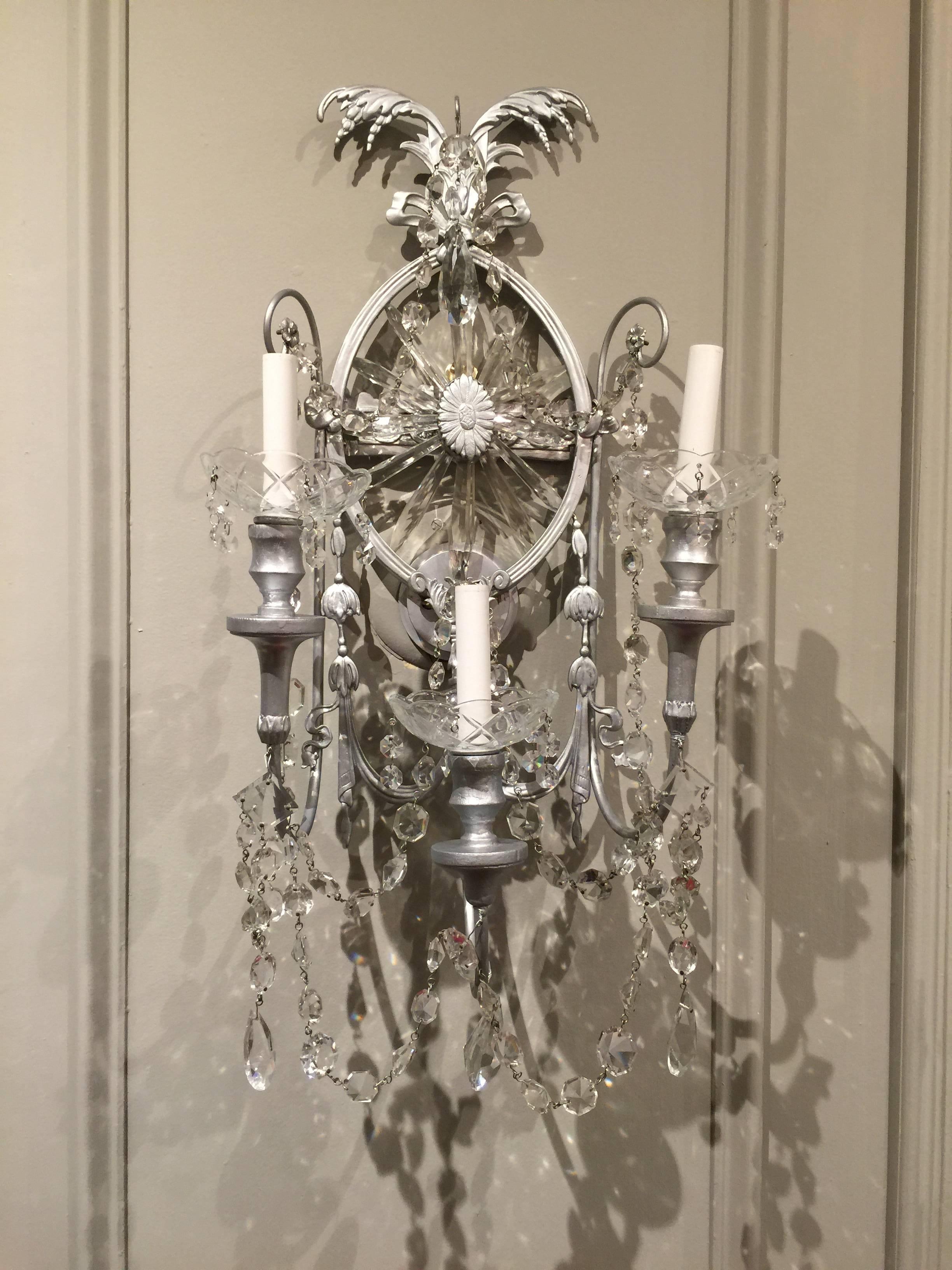 Gorgeous pair of neoclassical wall sconces. Each one of large-scale, silvered metal, and fitted with three lights and cascading crystal. Two pair of sconces are available.