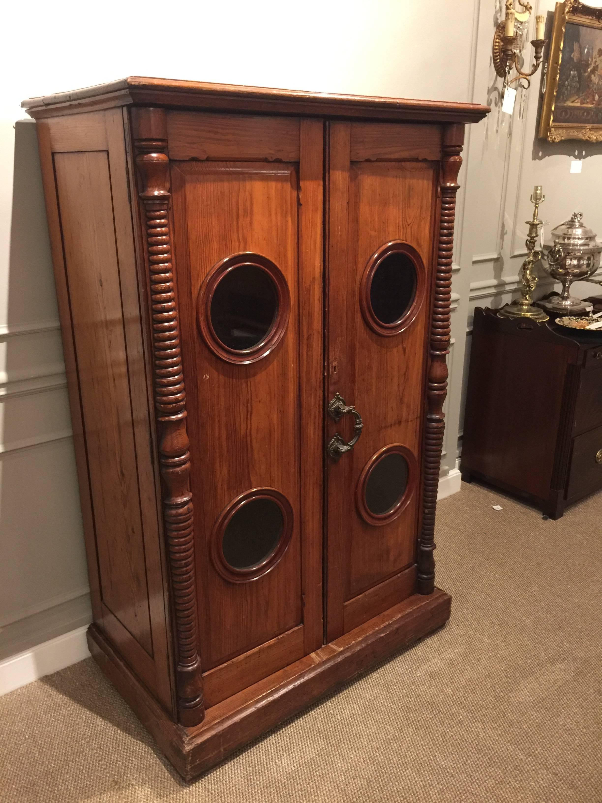 19th century Yacht cabinet, a rare find of antique ship furniture. The rectangular top over a case with flanking turned columns and two 18 x 54 inch doors each one fitted with two 7 inch portholes and a single cast bronze swing handle. There are two