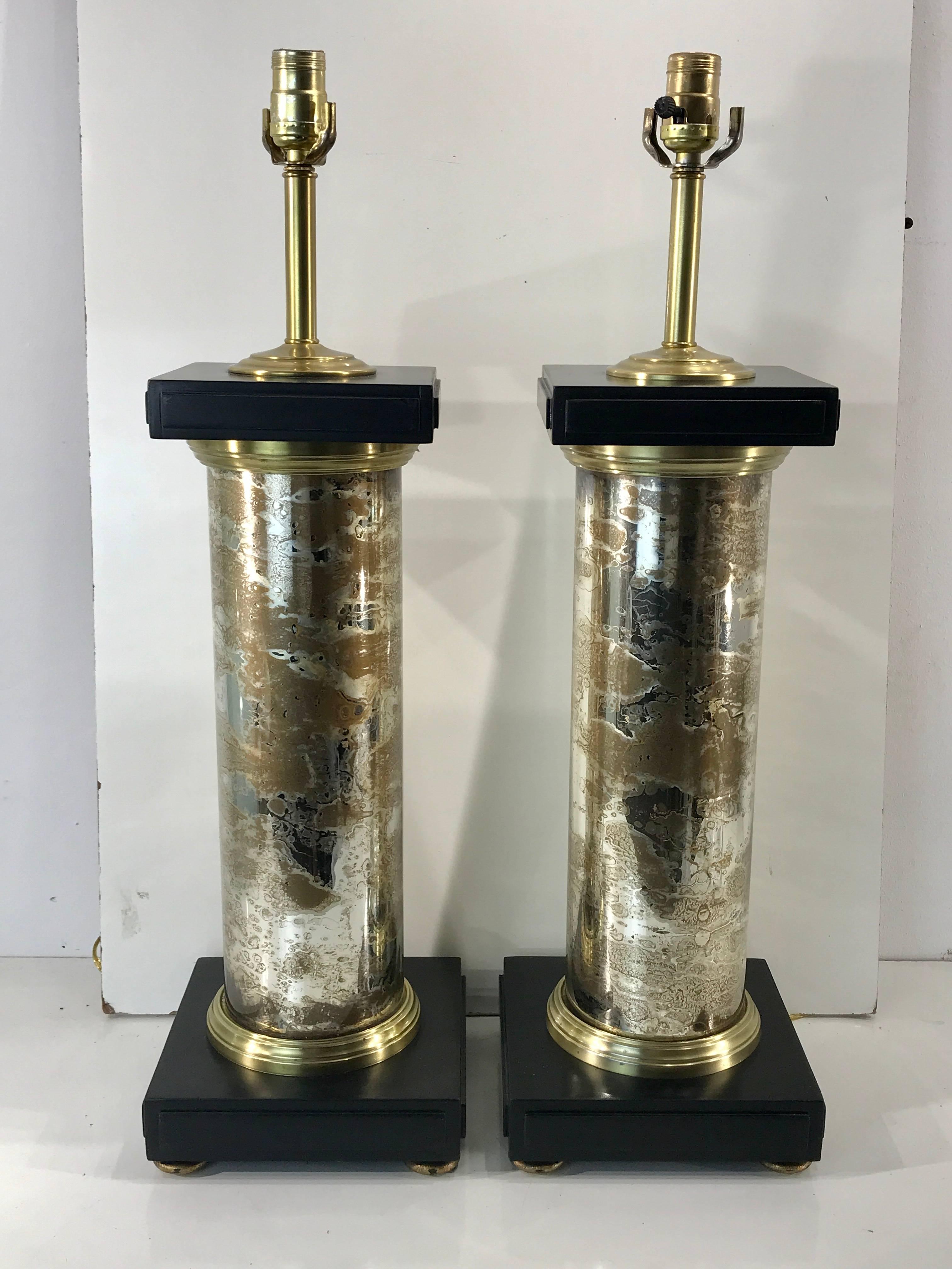 A pair of mercury glass column lamps, each one of great scale with carved and blackened square capitals with rich striated gold and silver mercury glass, resembling marble, reflective adding a greater sense of depth. 
Measures: 20" high to the