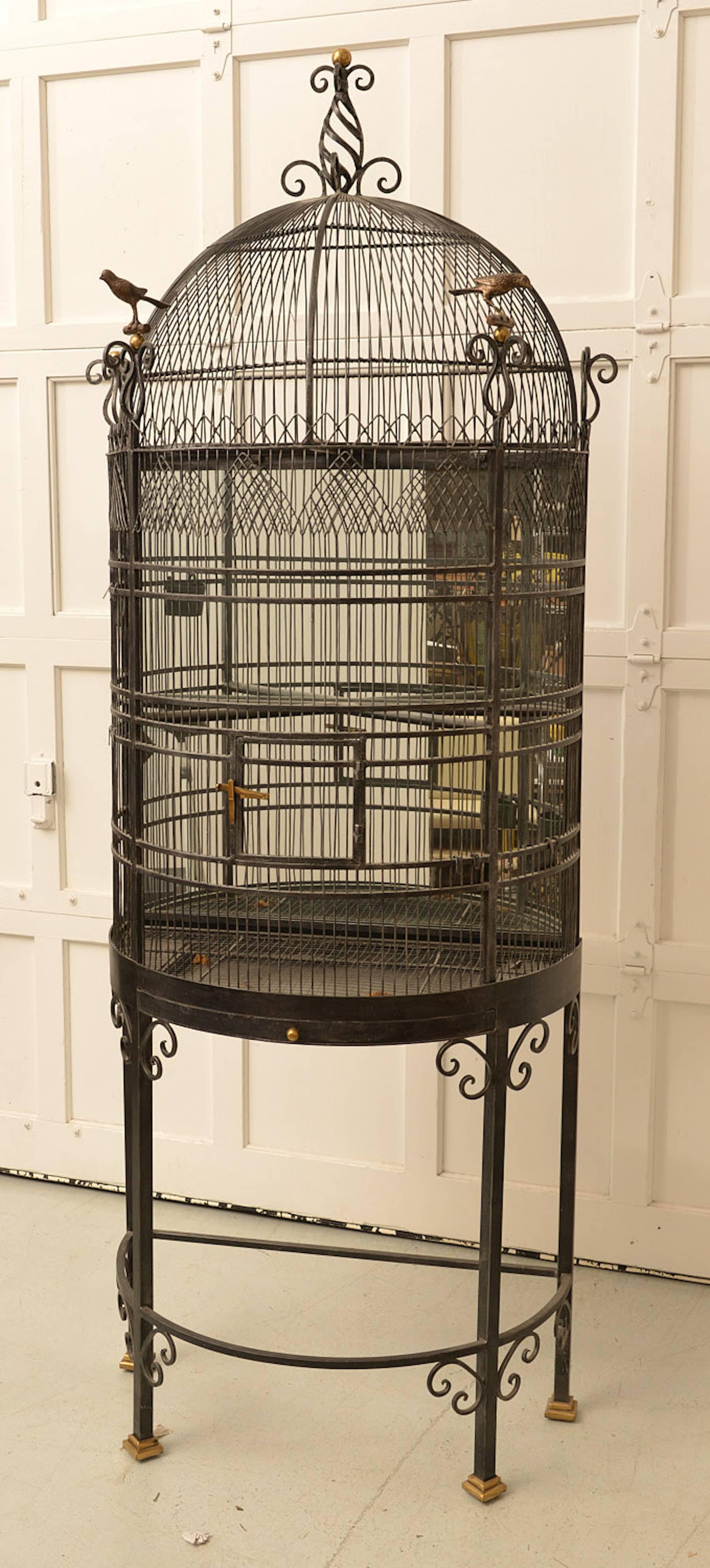 An elaborate brass and iron figural bird cage, of demilune form flanked by a pair of brass perched birds with a mirrored back. A fully functional and highly ornamented bird cage.