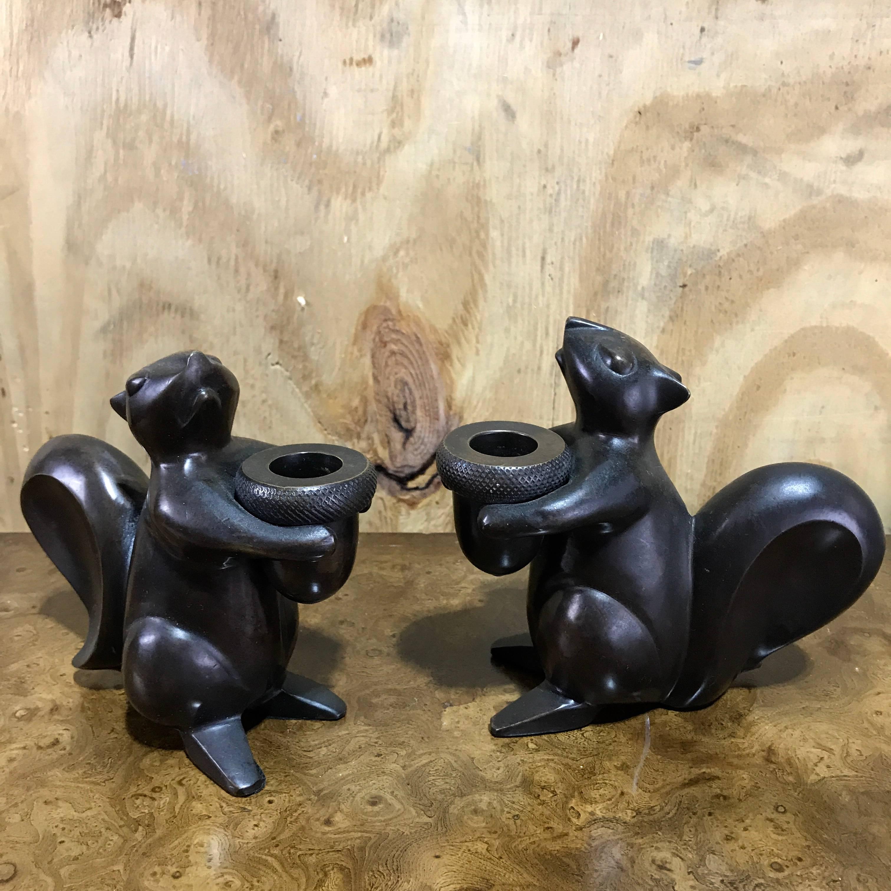 Pair of modern bronze squirrel motif candlesticks, each seated holding an acorn bobeche.