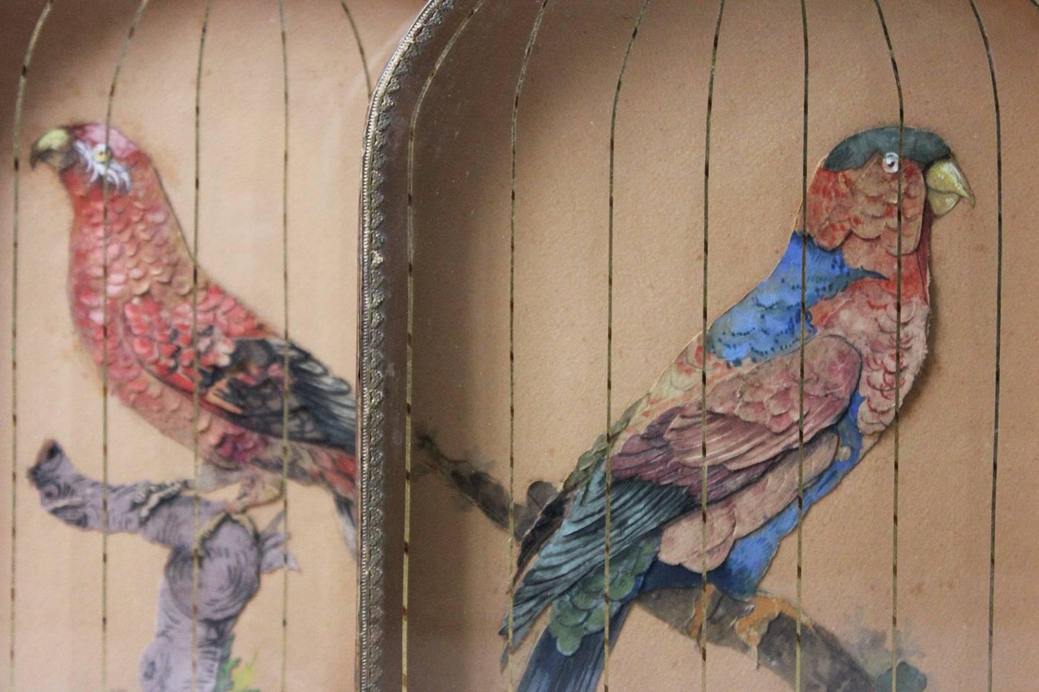 The beautiful and possibly unique, pair of opposing paper appliqué pictures of African parrots, each hand colored in paper and perching on water-color/gouache branches, the birds behind gilded threads mimicking the bars of a cage, each being glazed