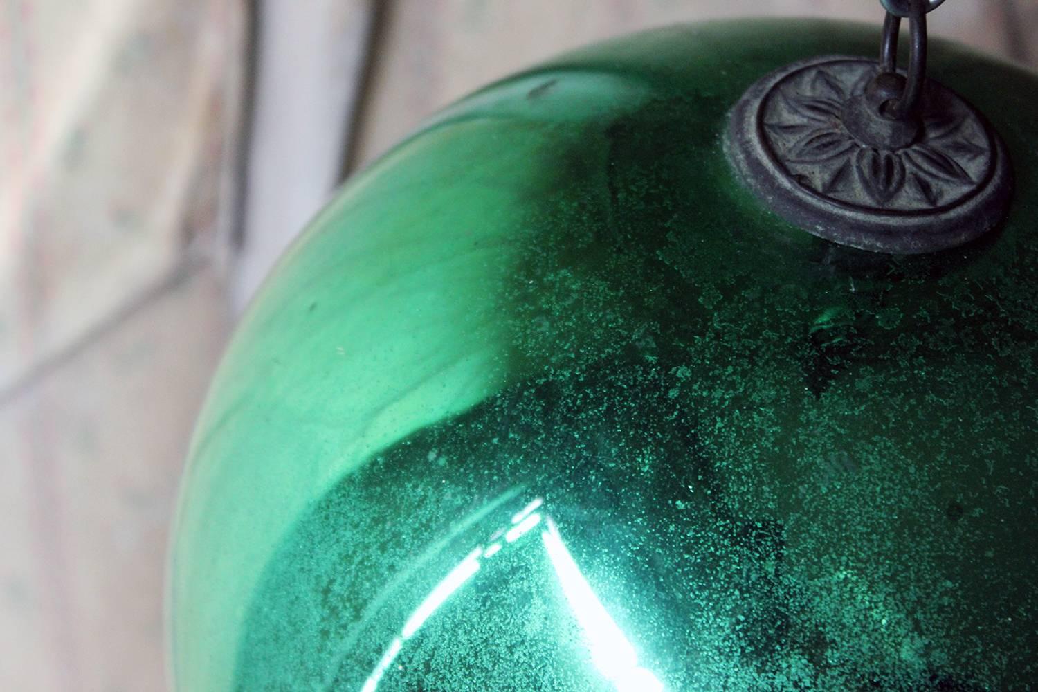 The handblown lustrous emerald green mercury glass witches ball, of large size, having the original hanging pressed loop crown attachment, and when hung reflecting an entire room, the whole showing a beautiful all-over patination, survives from the