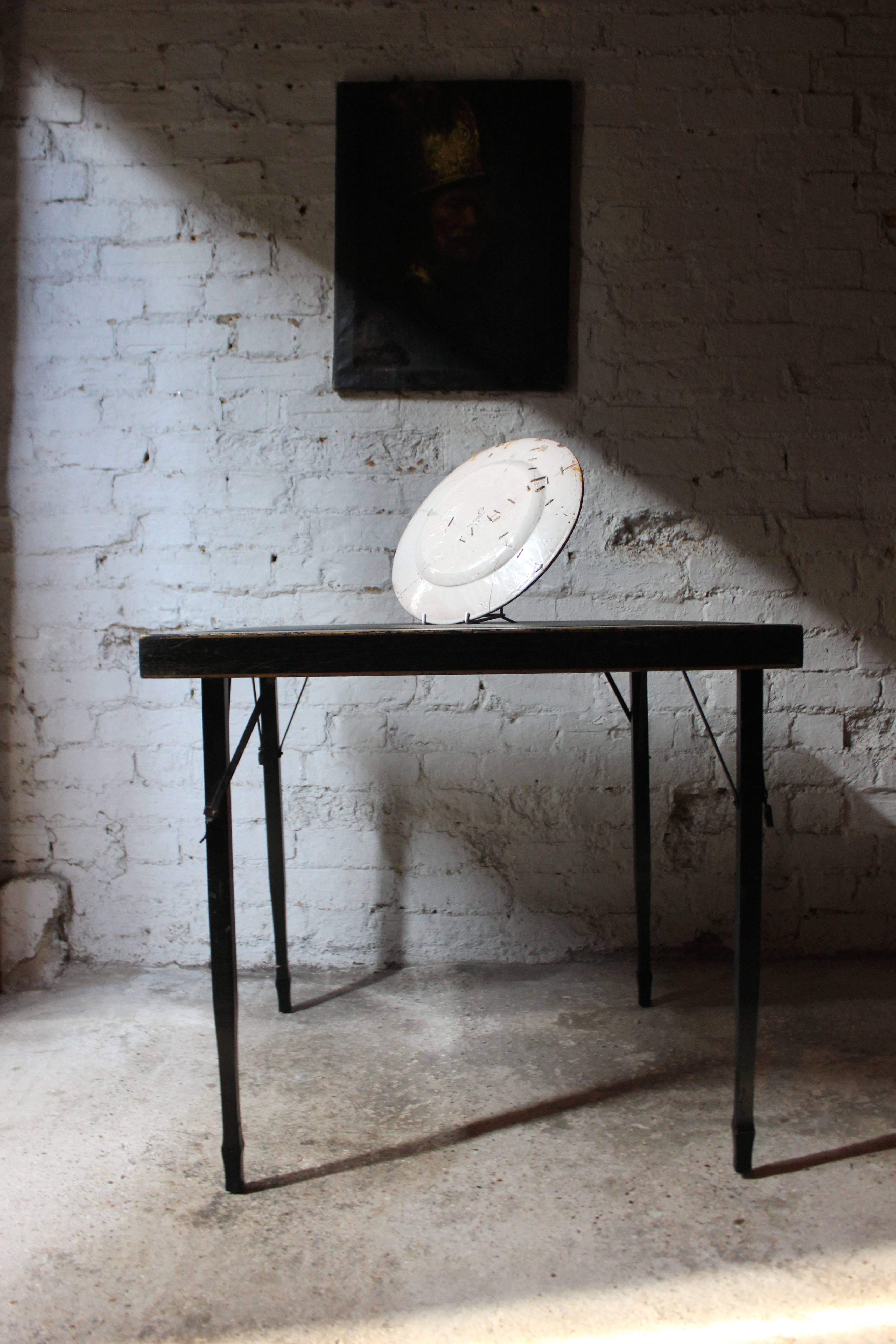 The early 20th century black lacquered transportable folding card table of square form, having an inset leatherette top with a gilded border depicting chinoiserie inspired motifs and scenes, on four tapering legs, and stamped to the underside