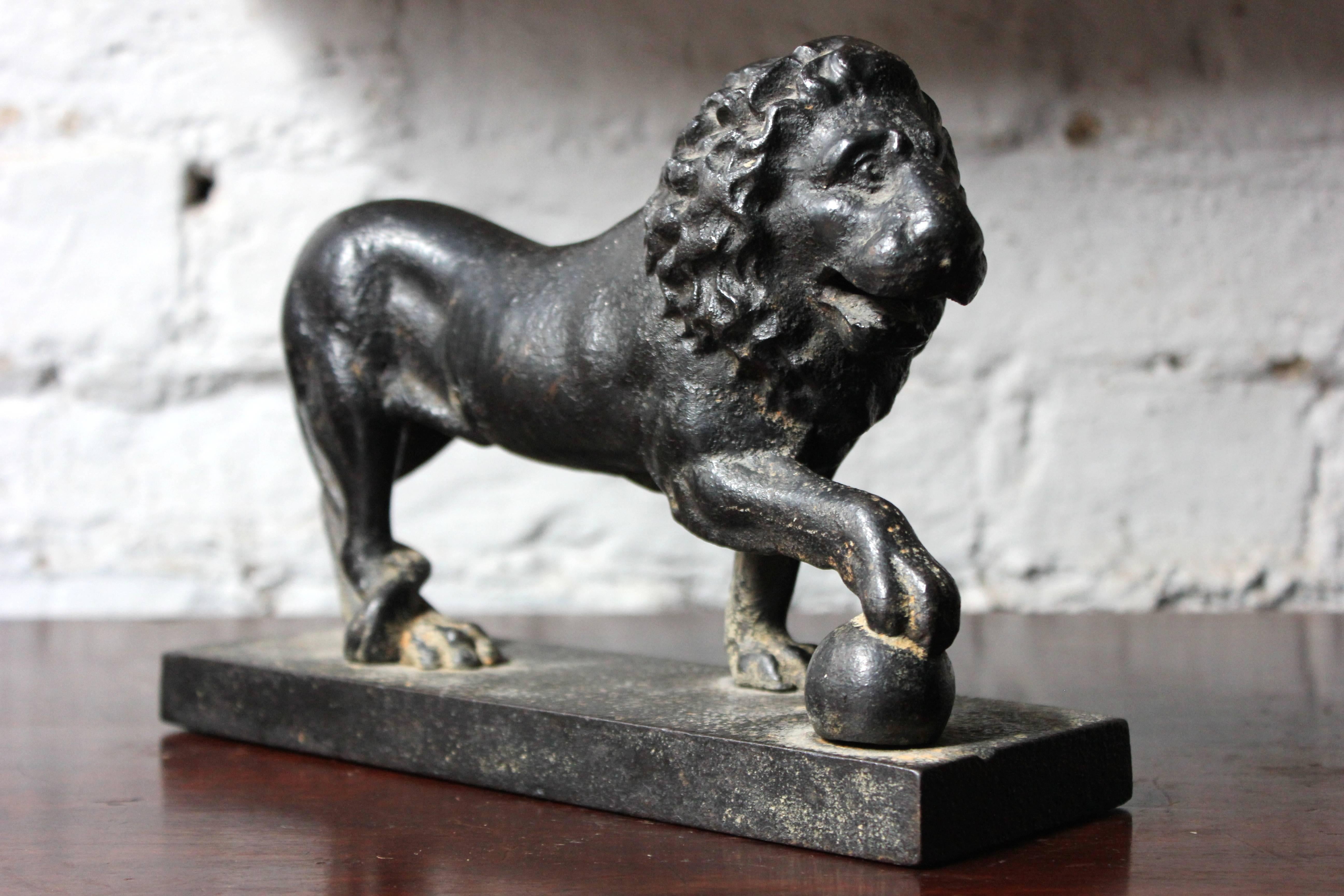 The heavy, tactile and wonderfully well-patinated cast iron door porter modelled as a Medici lion, standing on a rectangular base, the lion in the typical pose being a standing male lion with a sphere under one paw, looking away to the side, the