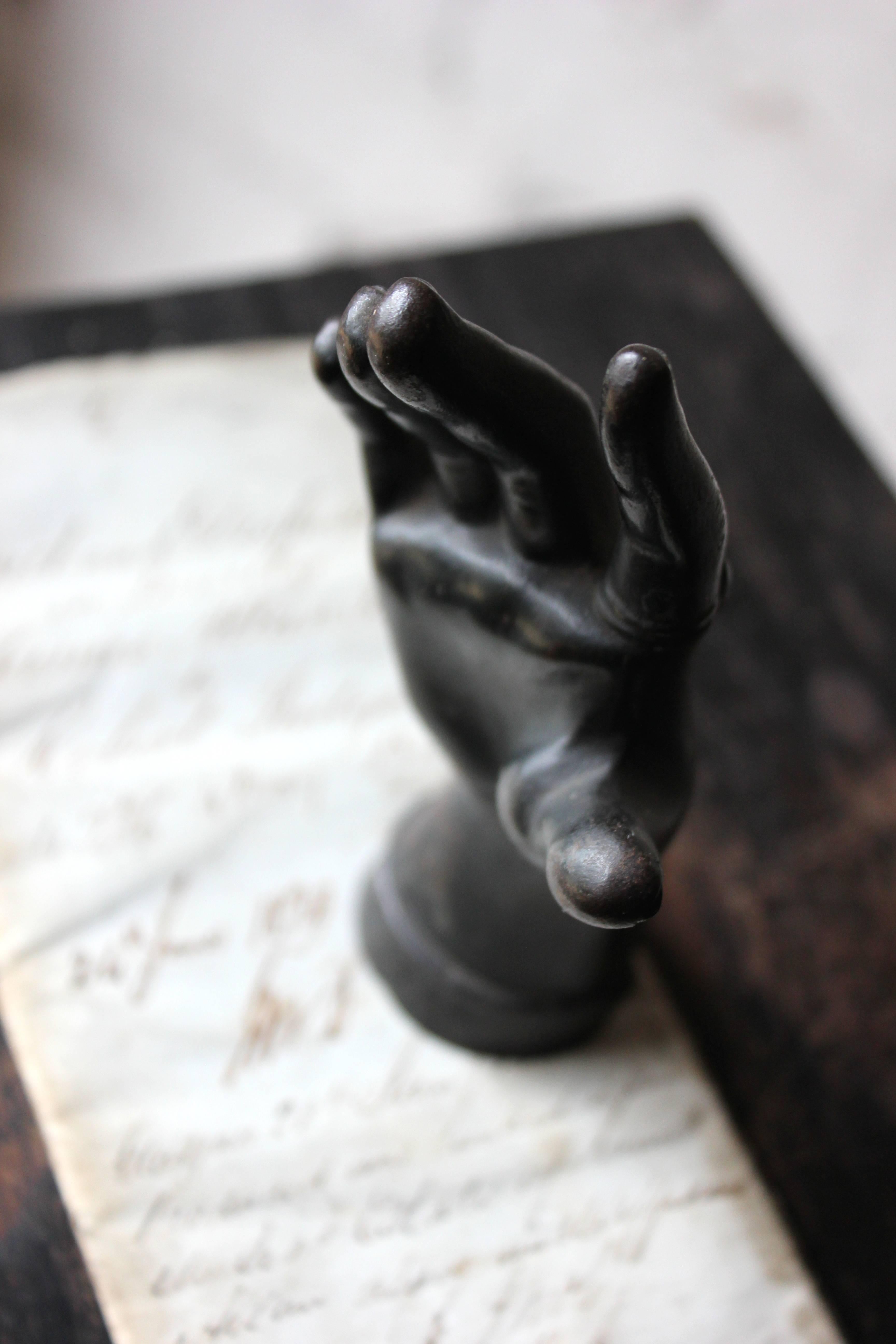 The good quality dark patinated cast iron novelty desk or paperweight, finely modelled as a dainty female hand to a bejewelled lace cuff, having a cabochon ring to the index finger and on a circular base, survives from high Victorian England.

In