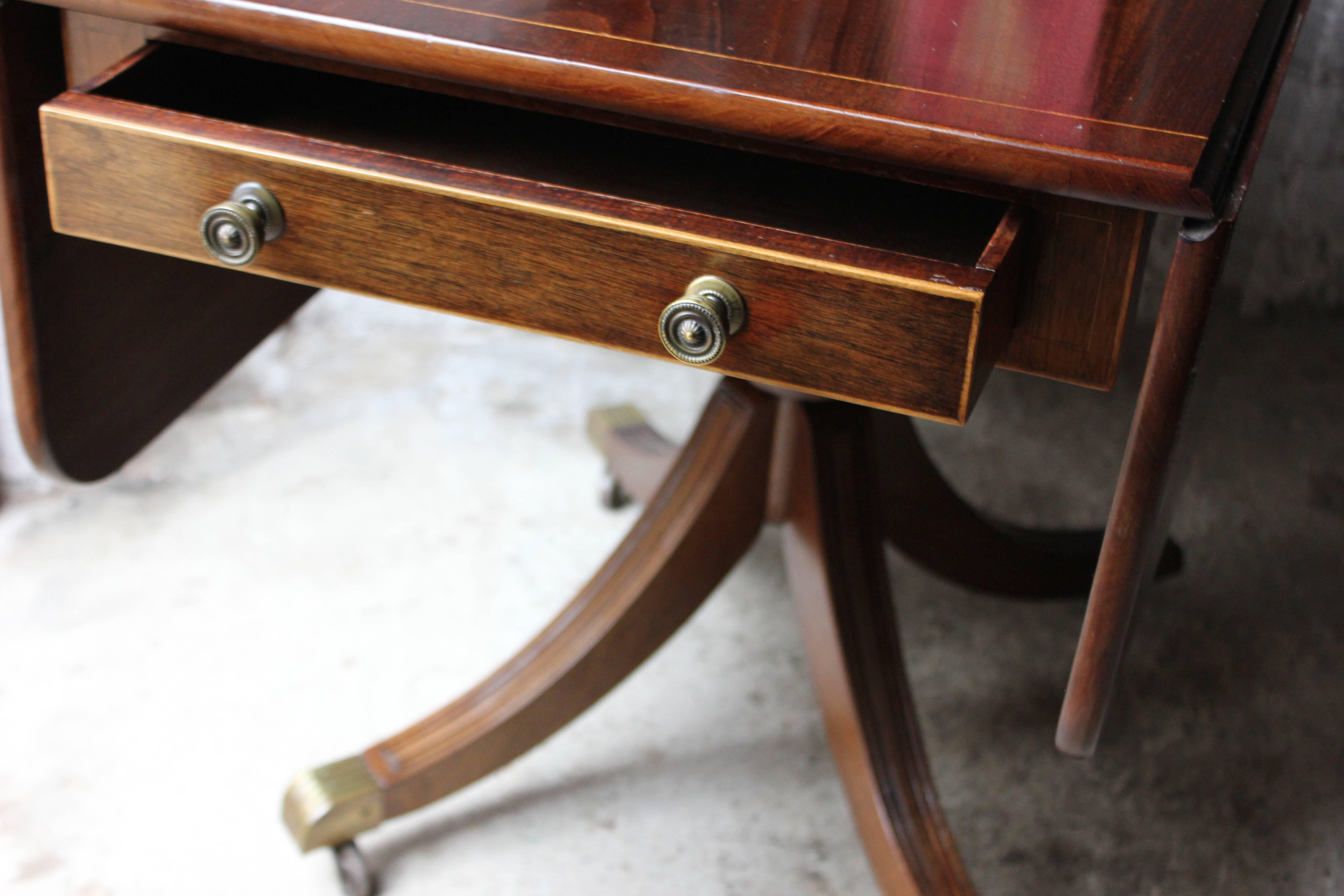 The Classic Regency period boxwood inlaid mahogany pedestal Pembroke table of good colour, having drop leaf sides over a frieze drawer, to a dummy at the opposing end, each being inlaid and with the original brass knob handles, the top raised on a