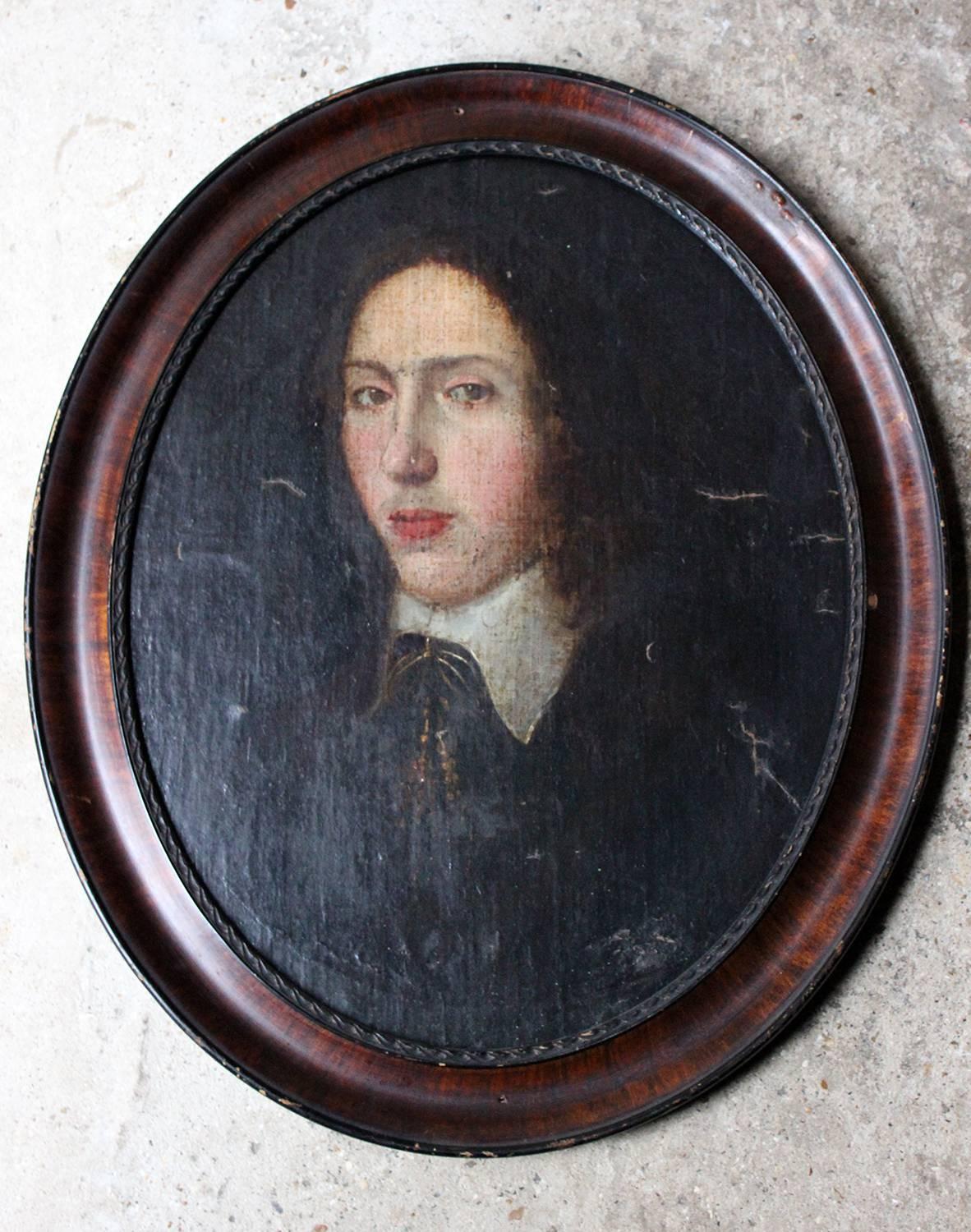 The half-length portrait in oval form of a dashing young French gentleman having long hair, and looking directly out to the viewer, painted in oils on canvas laid down to board, the sitter shown in a black over garment with a white collared under