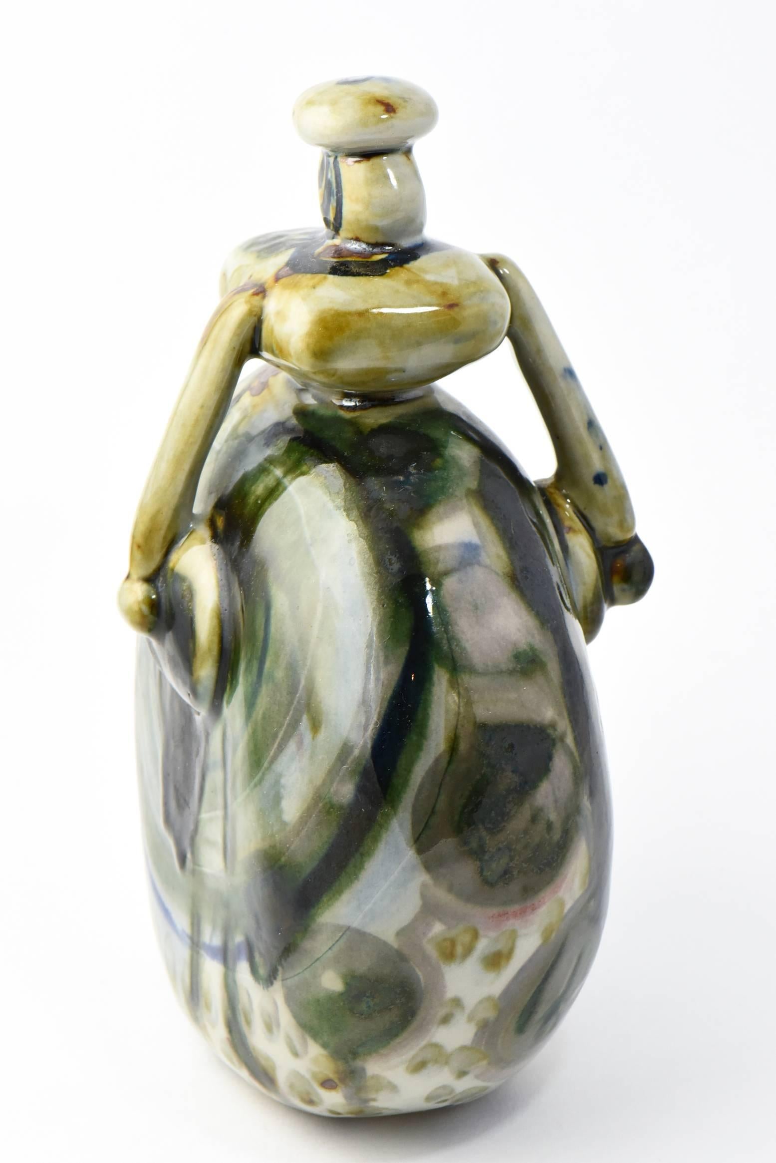 Ceramic figurine in the shape of a woman with green, blue, white and beige mottled glaze. Signed on base, but not fully legible.