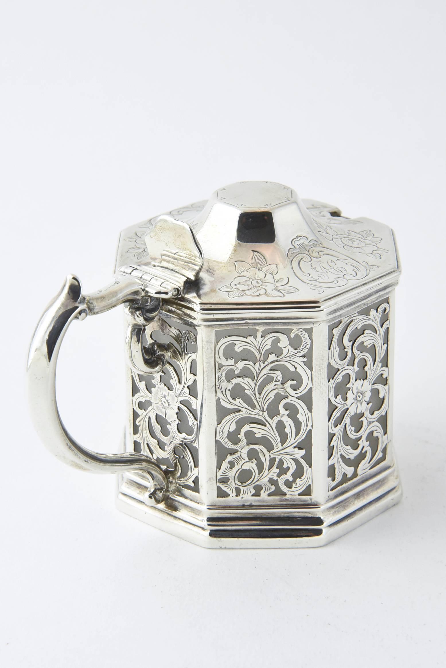 Fino recipiente inglés perforado de plata de ley y cristal blanco cubierto de flores para mostaza, Londres, 1848 Fabricantes: John Angell y George Angell. El cuerpo es un diseño floral perforado de esterlina y la parte superior lleva grabado un