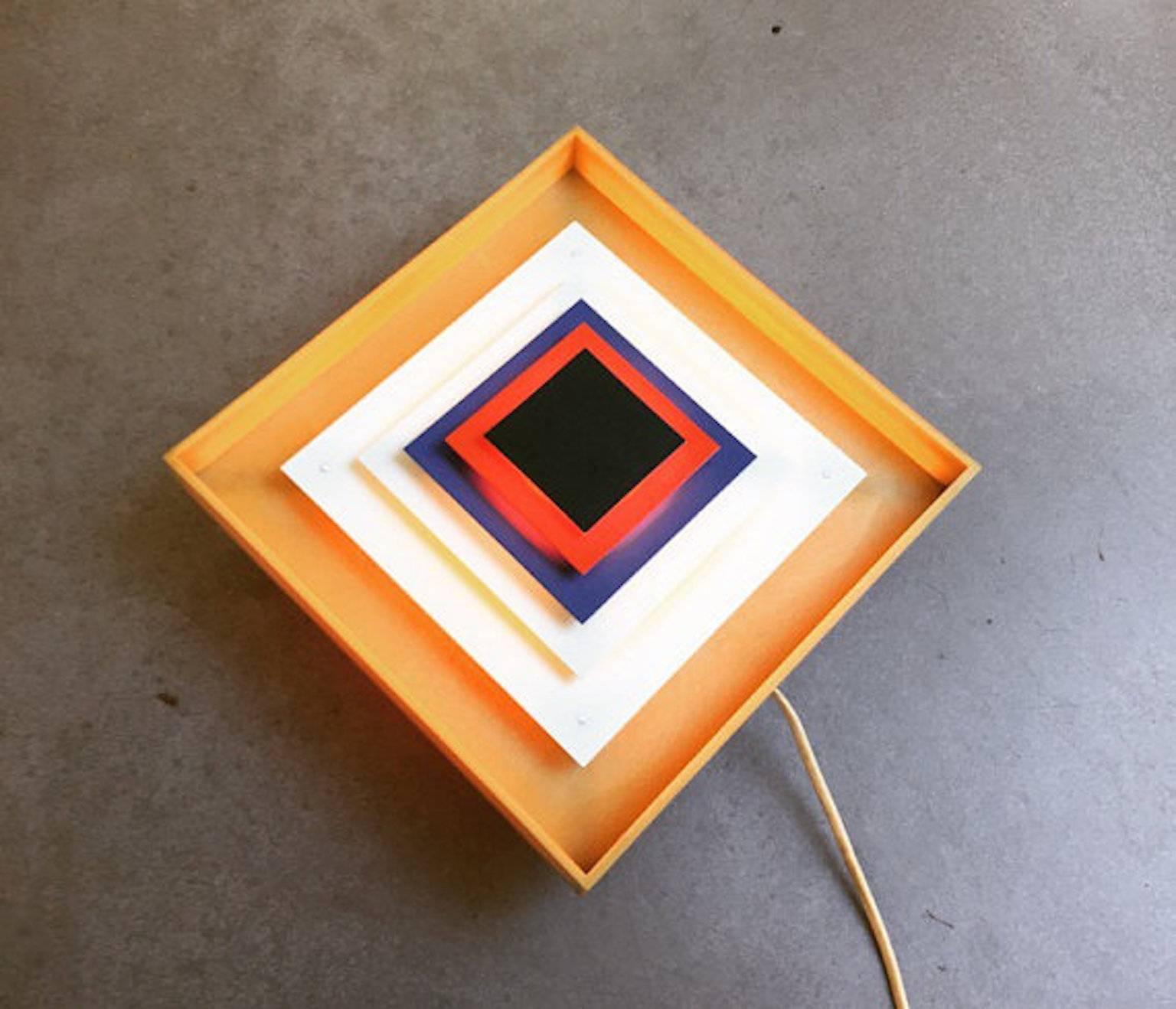 Rare designer sconce from Danish Lyfa designed by the world known Bent Karlby.

Op-art wall lights with layered back-lit metal squares made with a plastic frame and painted metal squares. 

This light is designed for multiply use - on a shelf,