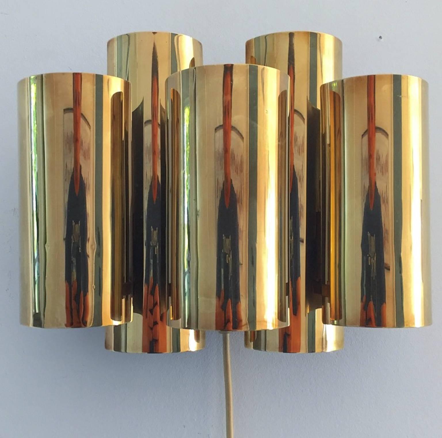 This beautiful brass wall sconce with five cynlidrical shades was designed by Danish light designer Svend Aage Holm Sørensen. 

He is known for his Brutalist lamps but this is a very beautiful elegant lamp from his hand- a rare design indeed from