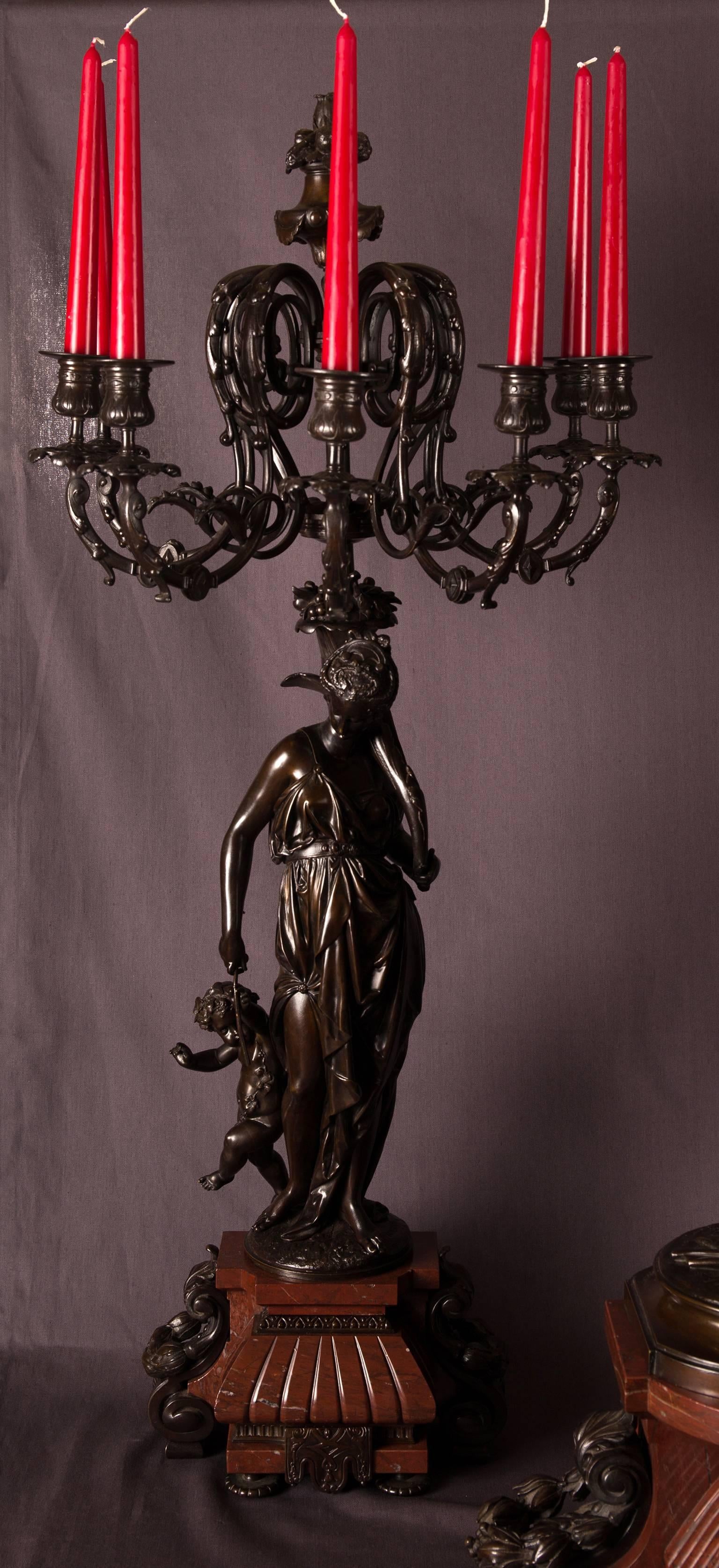 Impressive patinated bronze mantel clock garniture representing Daphnis and Chloe on top of the clock and a pair of seven-light candelabra each with a nymph and putto that hold the candleholders, coming out from cornucopia. The bases are made of